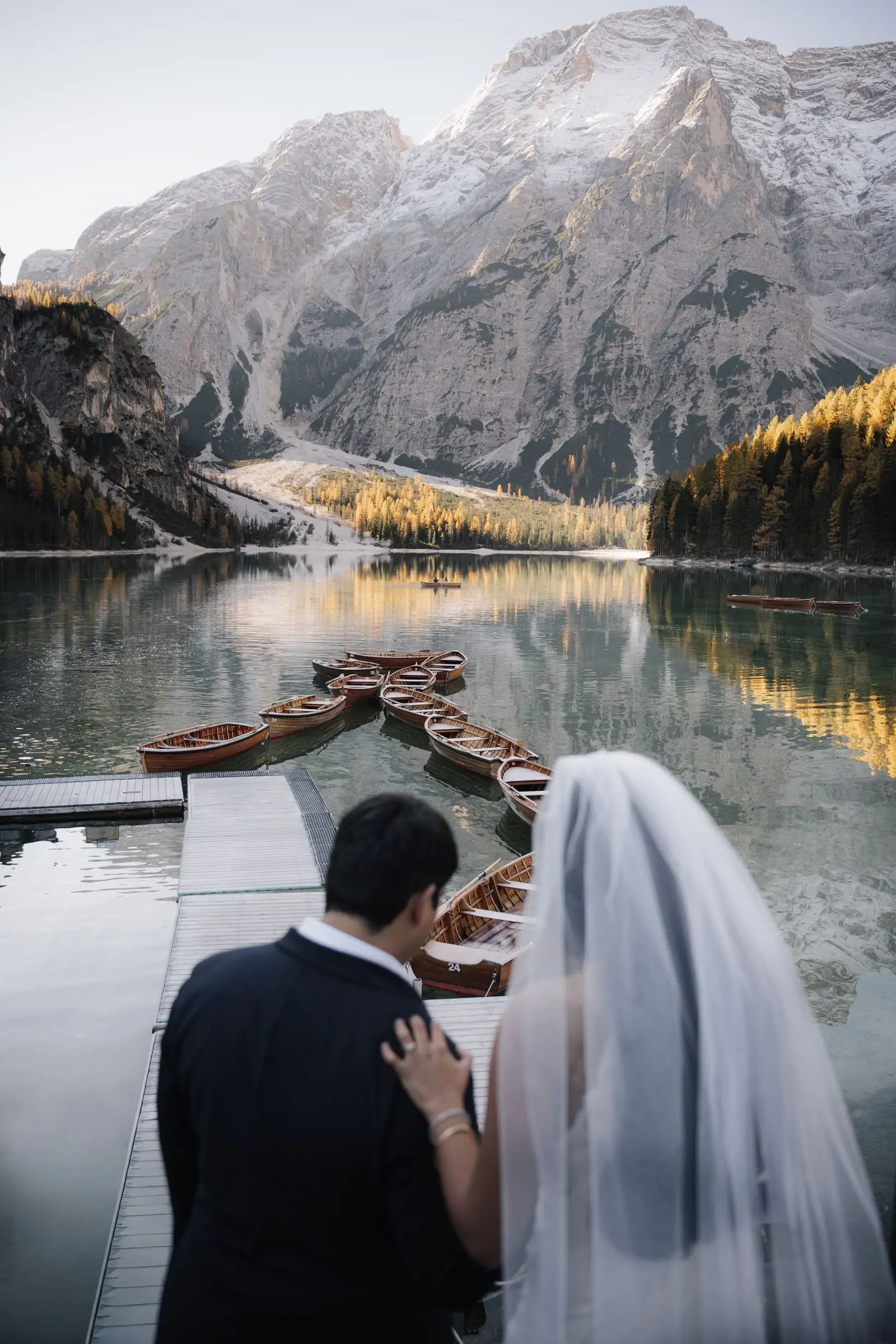 Couple on the jetty overlooking the wooden boats and autumn larches of Lago di Braies