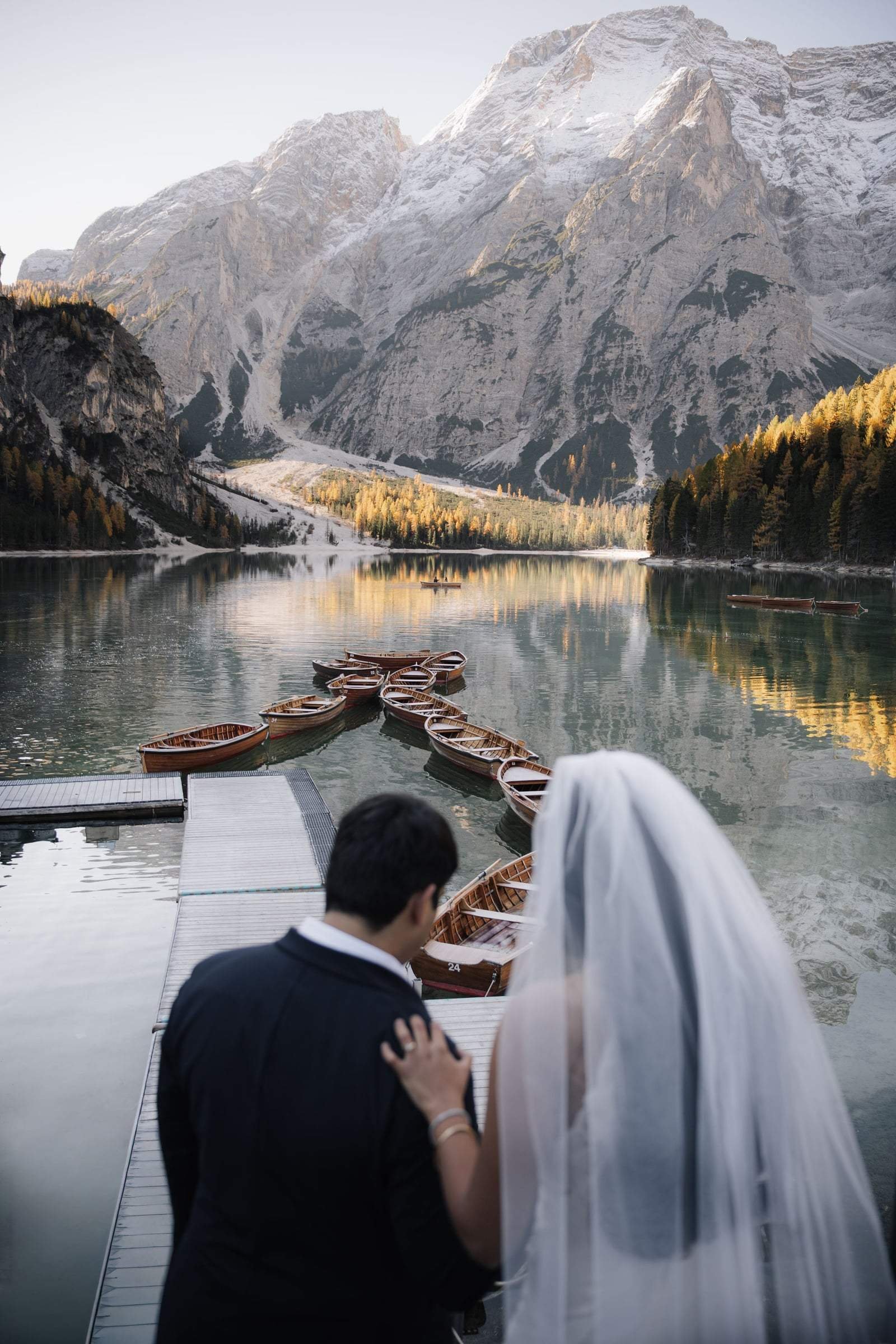 Couple on the jetty overlooking the wooden boats and autumn larches of Lago di Braies