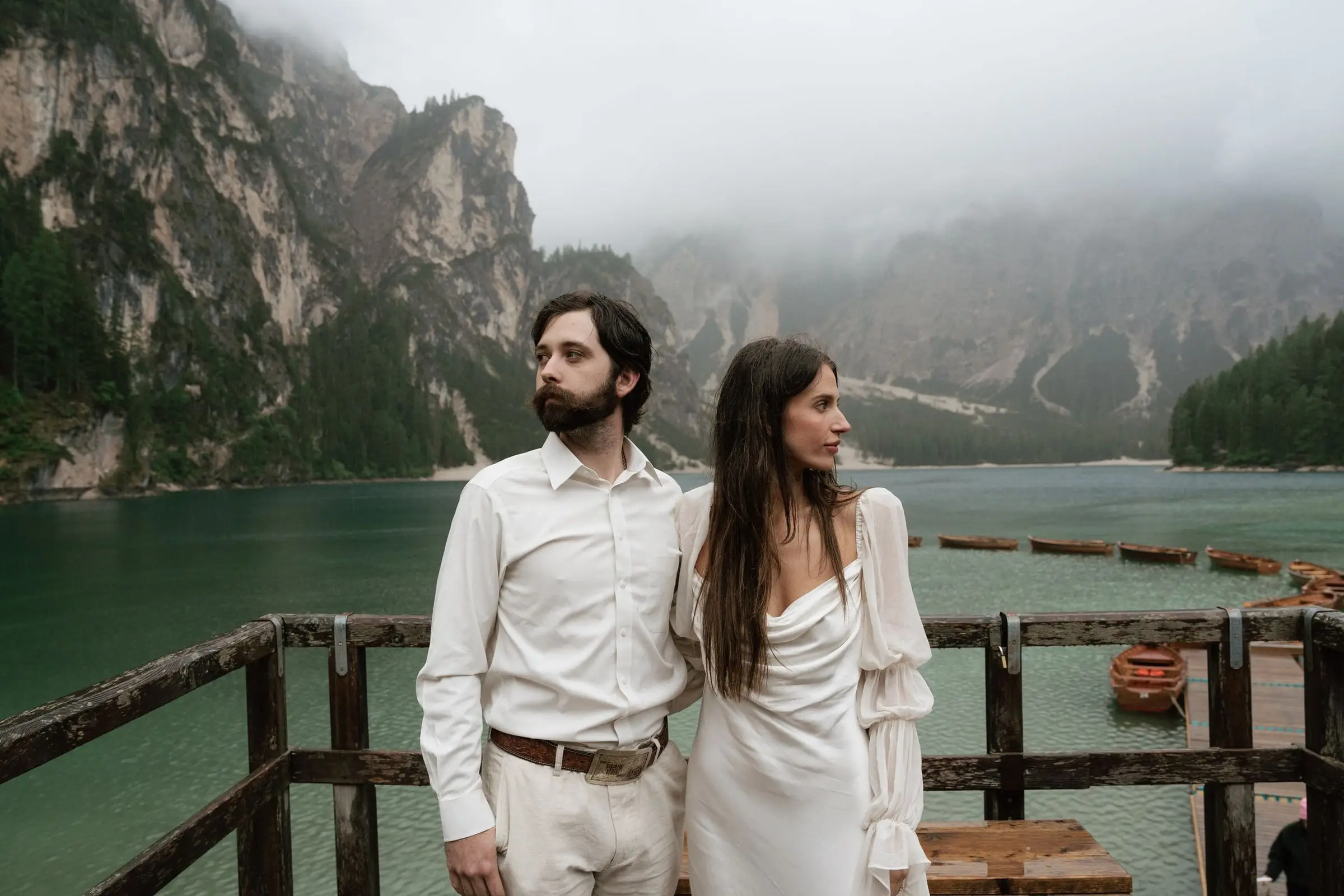 Couple in white on the boathouse terrace at Lago di Braies, mist over the mountains