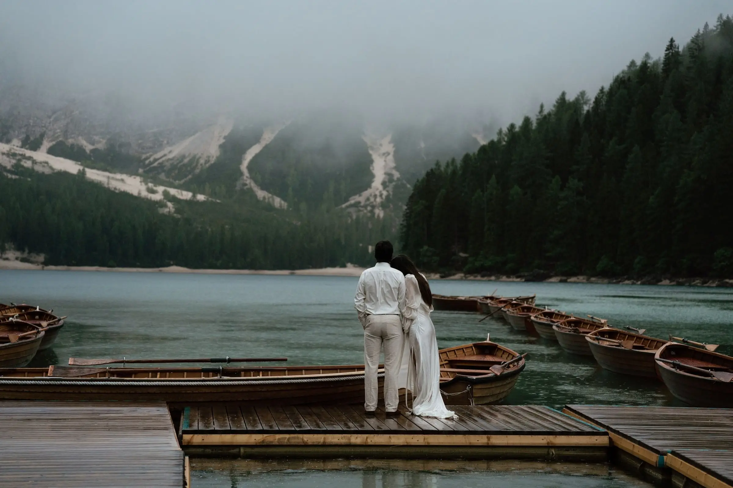 Couple on the wooden jetty looking over the misty lake and the rowing boats