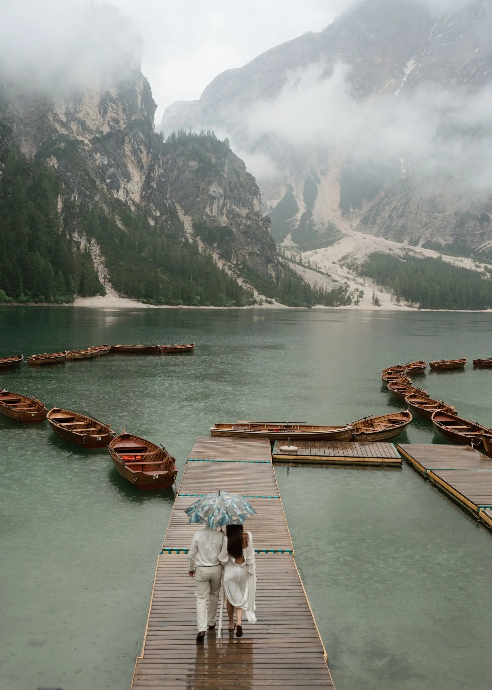 Couple under a clear umbrella walking down the jetty between the boats in the rain