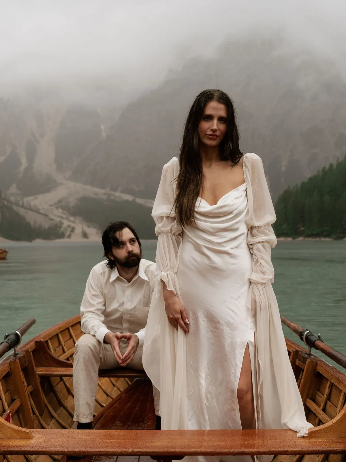 Bride standing in the rowing boat, the groom seated, cliffs in the mist