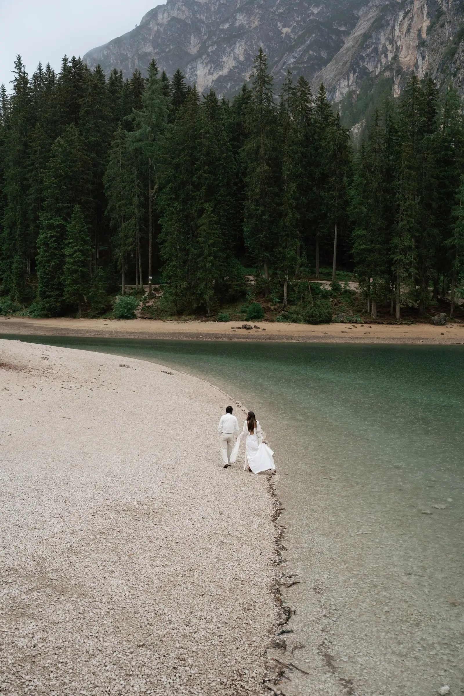 Couple walking along the pale pebble shore of the lake
