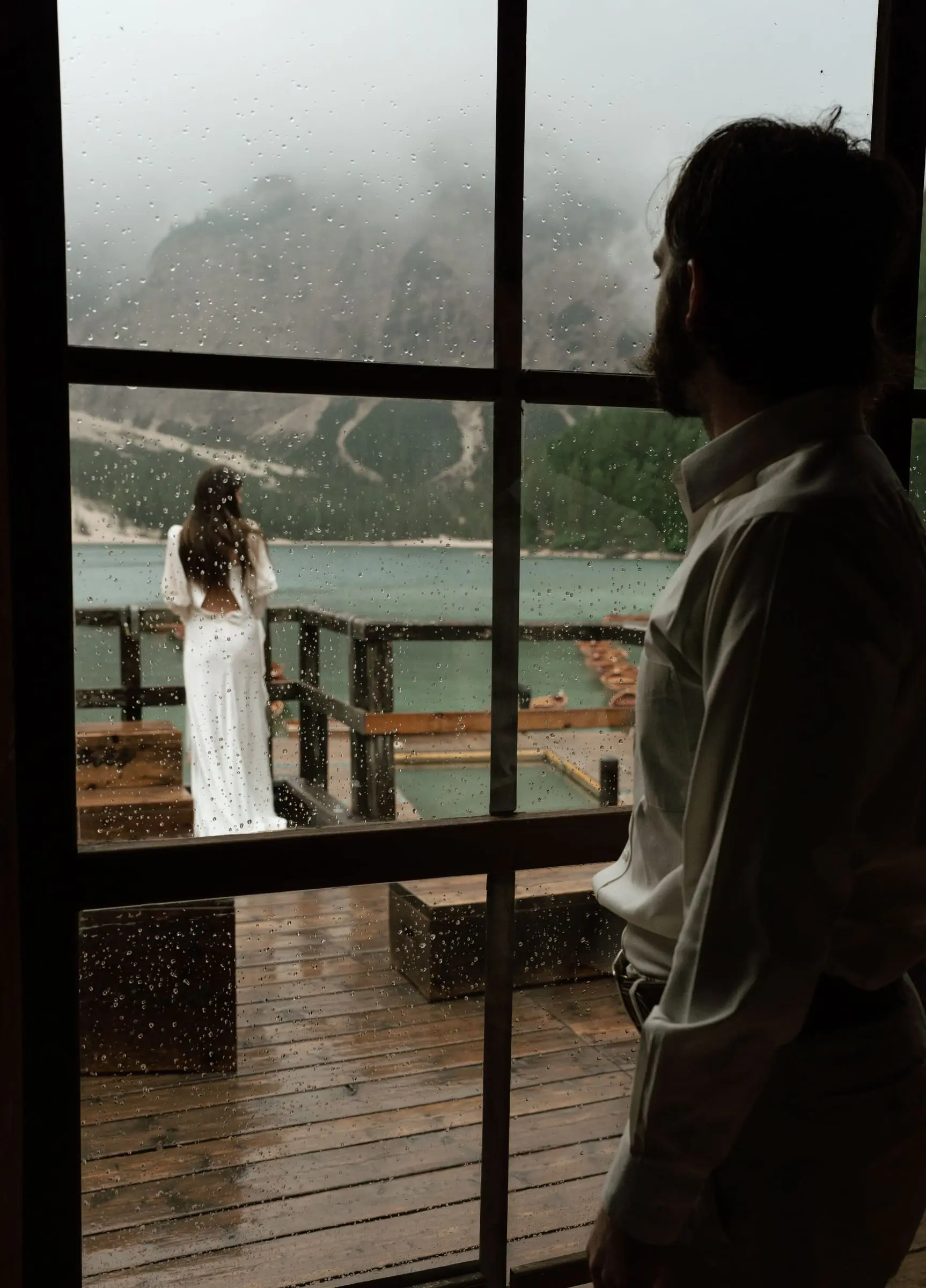 Bride on the terrace seen through the boathouse window, the groom in the doorway