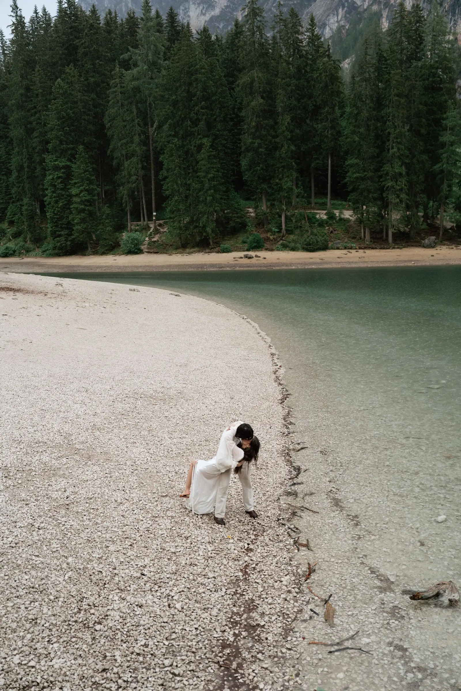 Couple kissing on the pebble shore, the forest behind