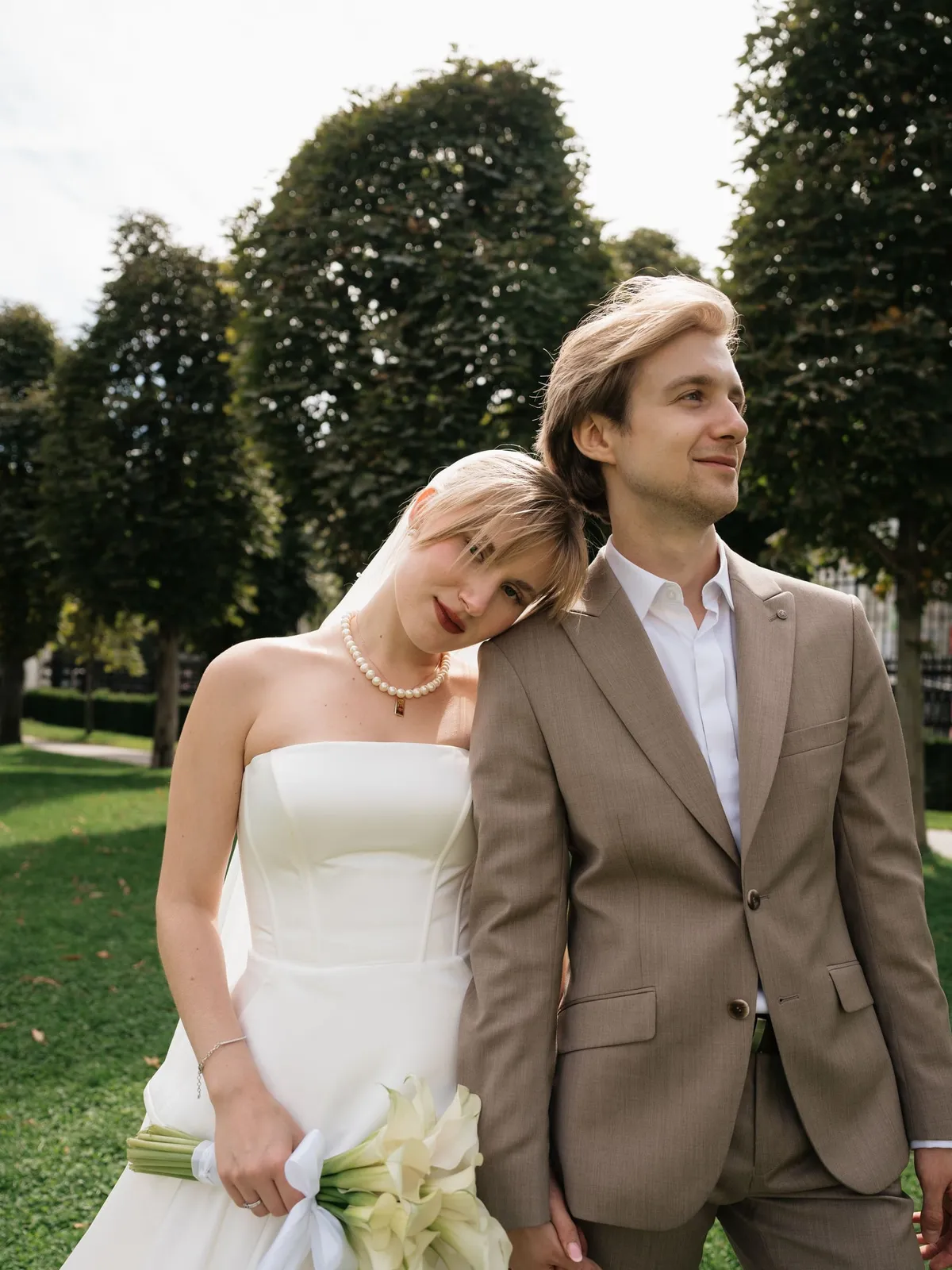 Bride leaning on the groom's shoulder in a Vienna park, calla lilies in hand