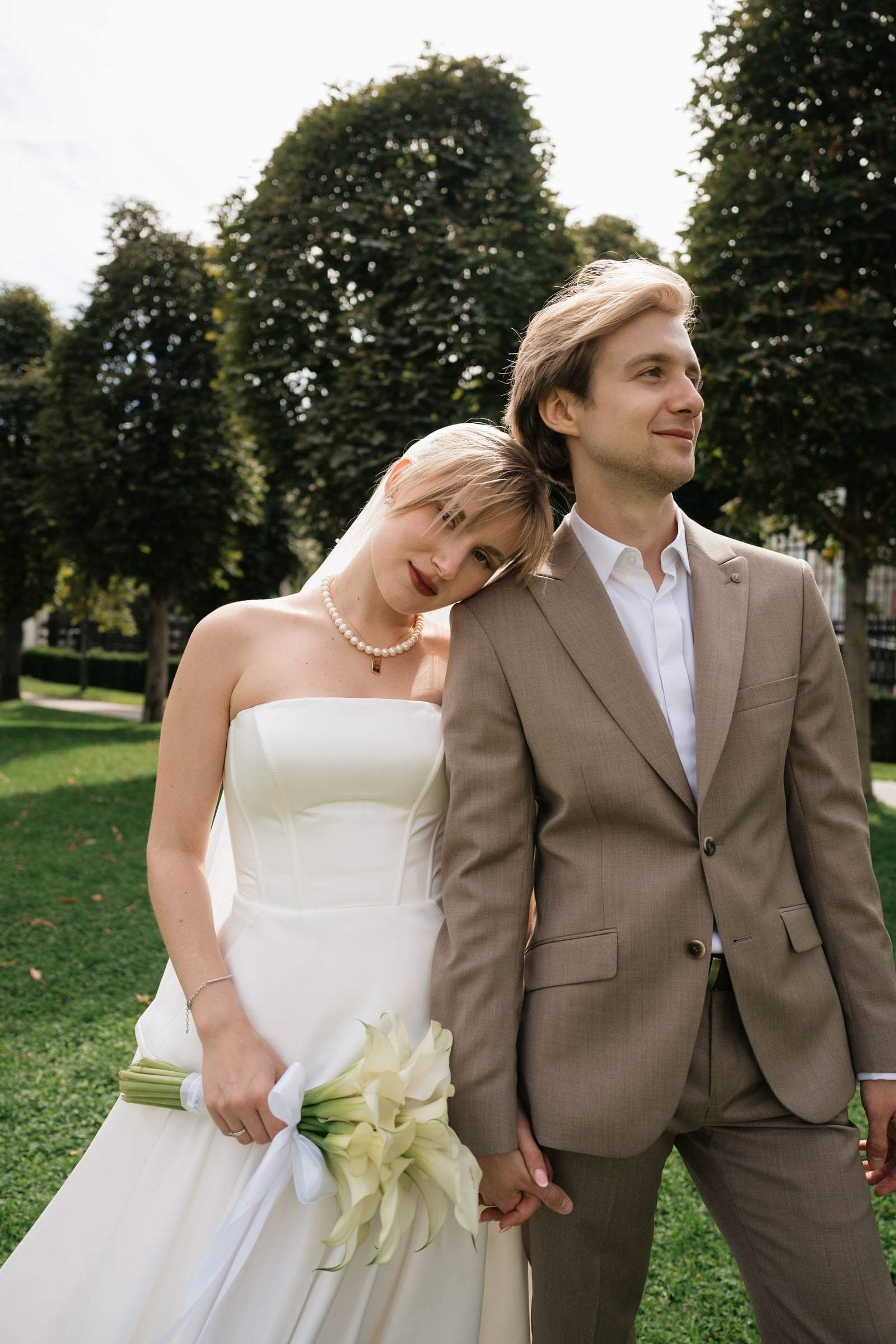 Bride leaning on the groom's shoulder in a Vienna park, calla lilies in hand