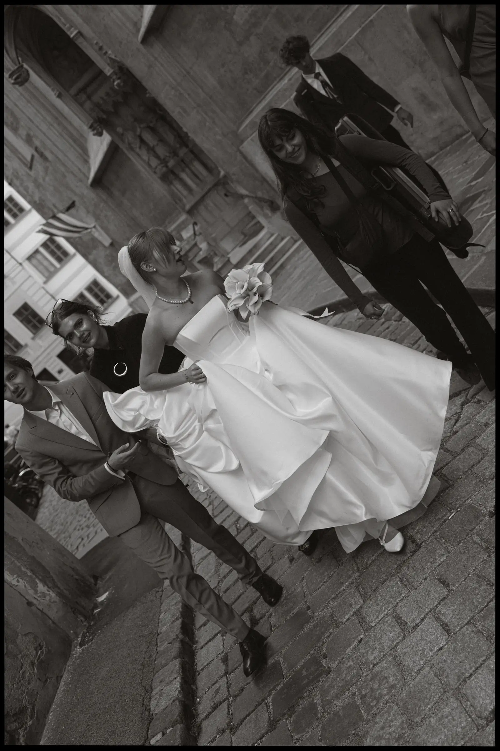 Black and white photo of the bride lifting her gown on the cobblestones, on film