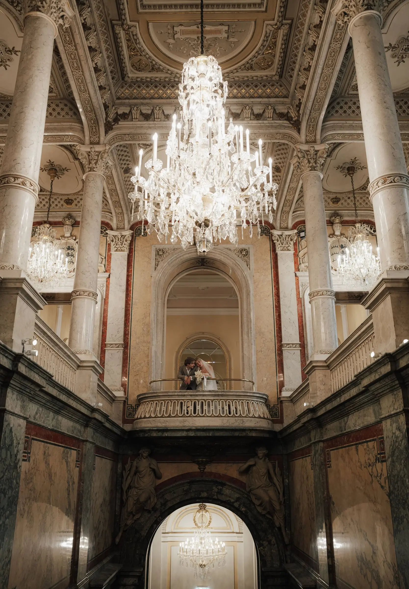 Couple on the balcony of a grand marble staircase with a crystal chandelier in Vienna