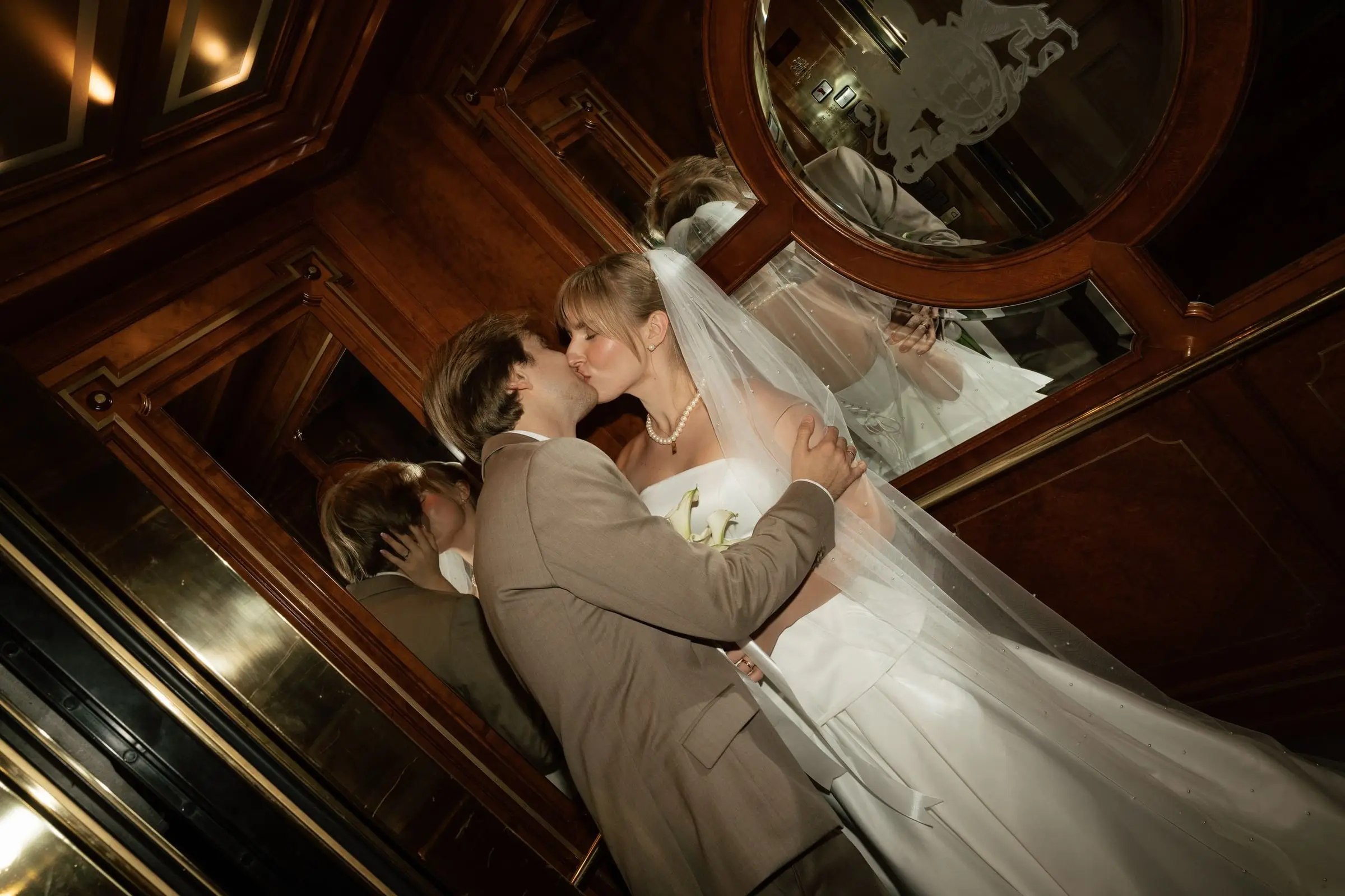 Couple kissing in a wood-panelled lift, reflected in the mirror