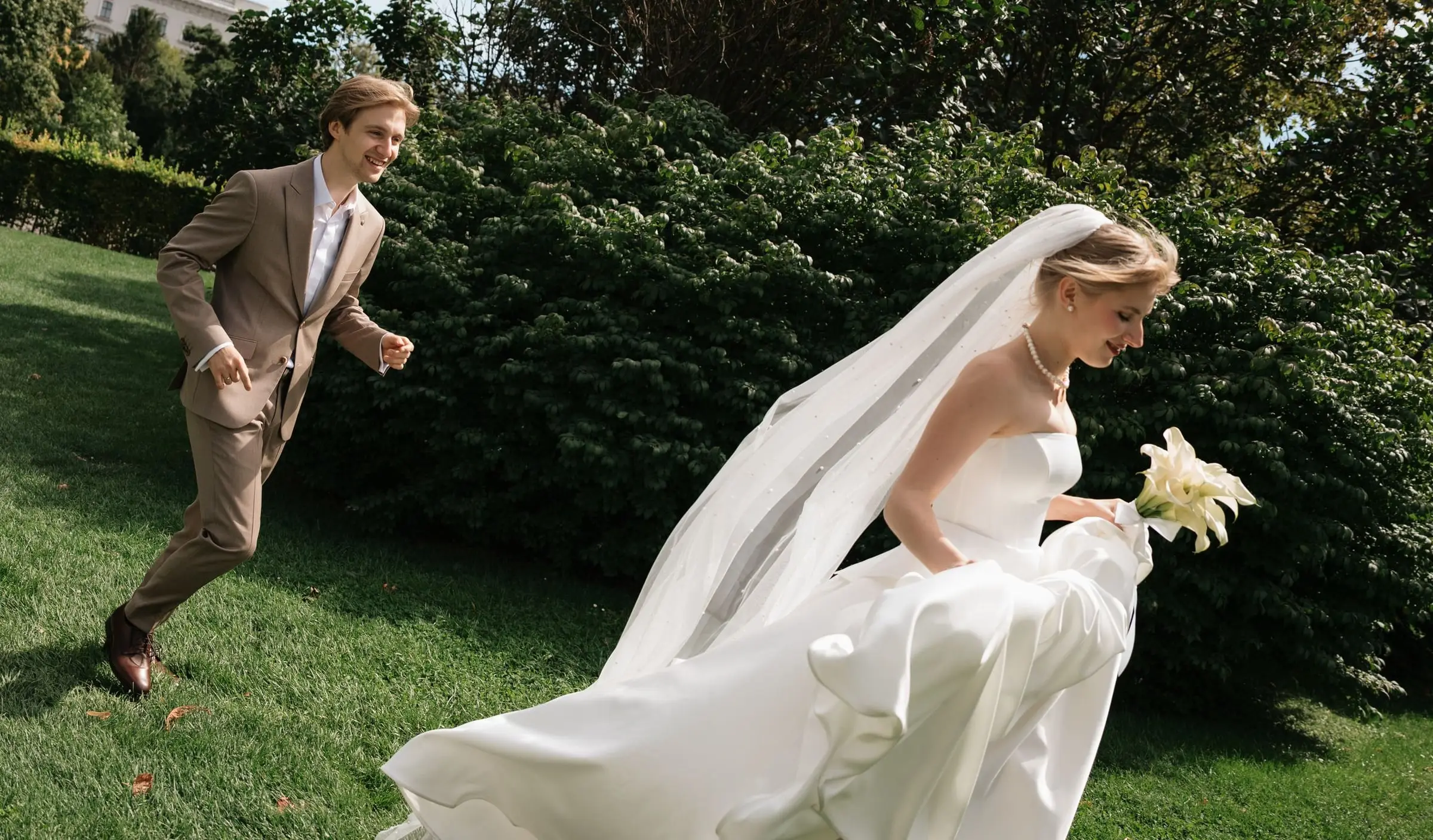Groom running after the bride across the lawn, her veil flying