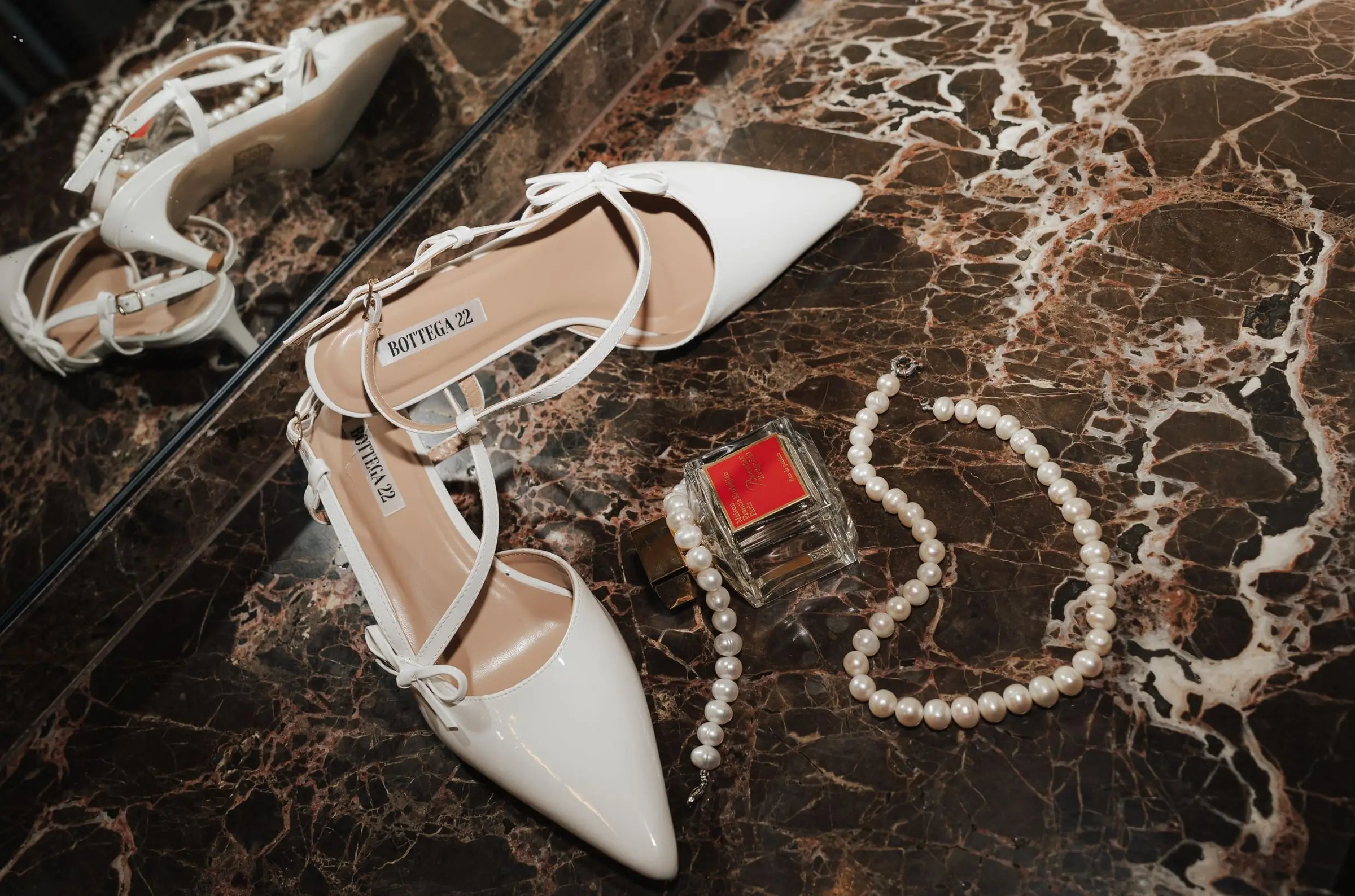 Bridal shoes, a pearl necklace and a red lipstick on marble