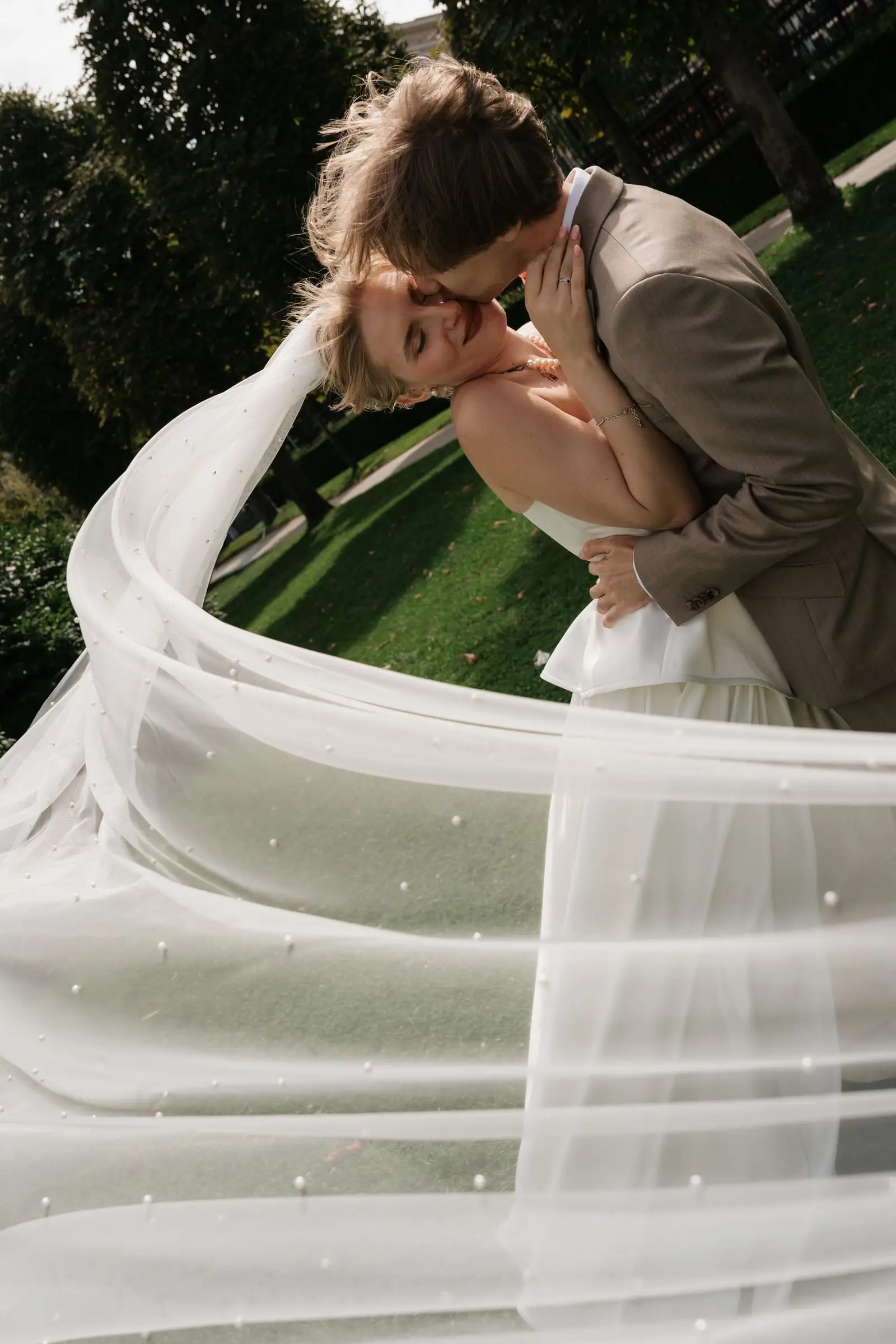 Couple kissing in the park, her long veil swirling around them
