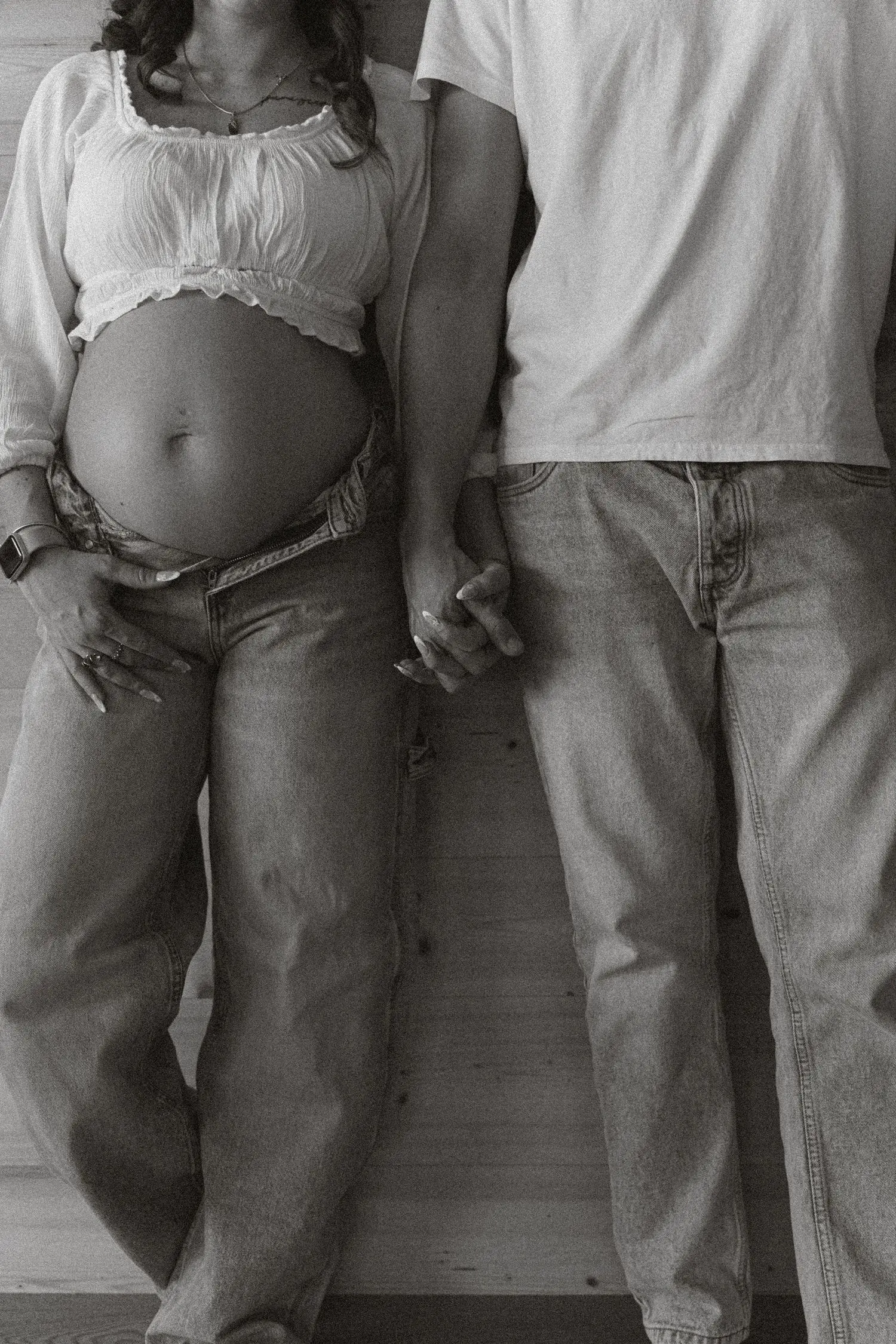 Black and white detail of a pregnant belly and the couple holding hands