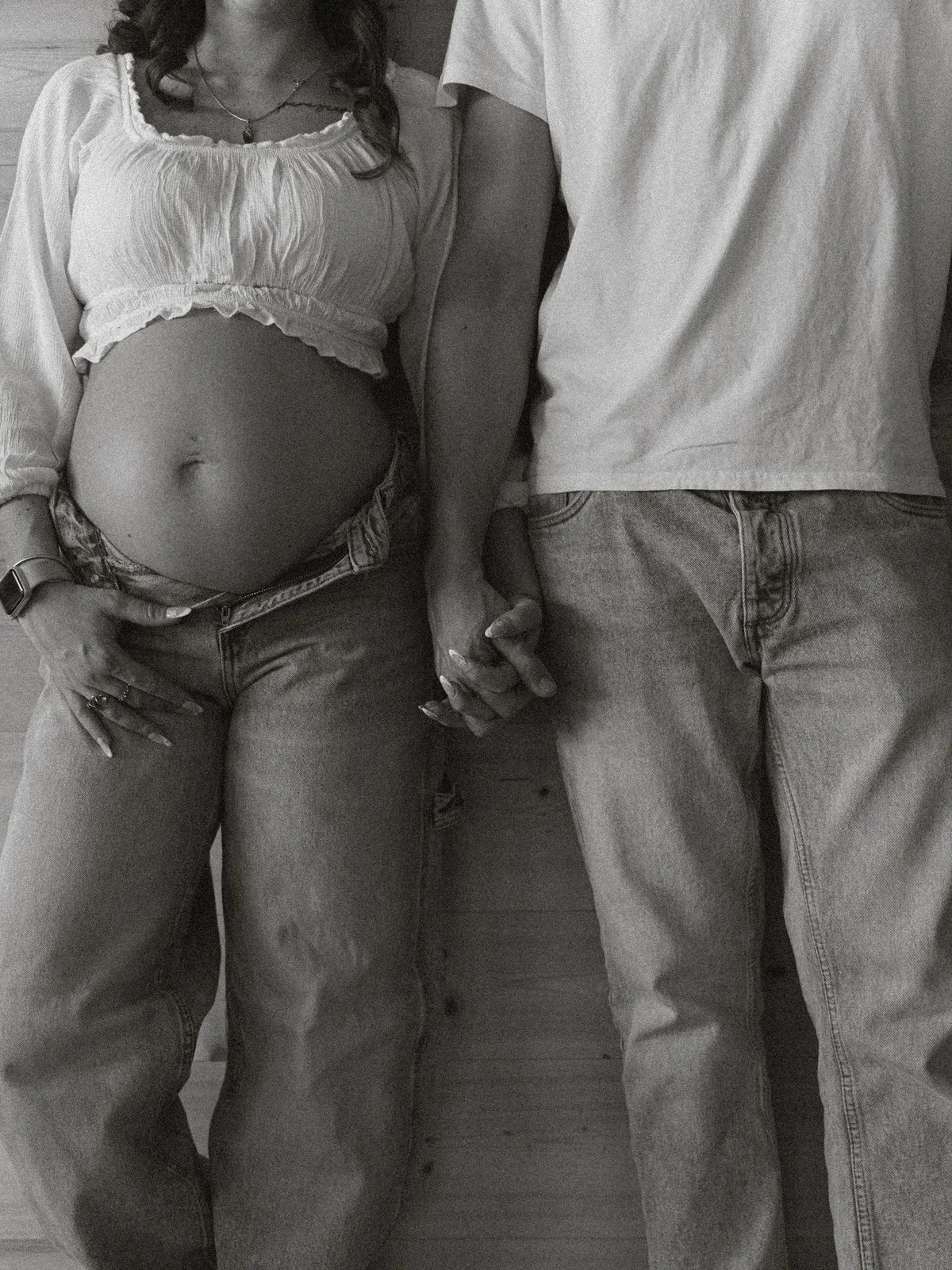 Black and white detail of a pregnant belly and the couple holding hands