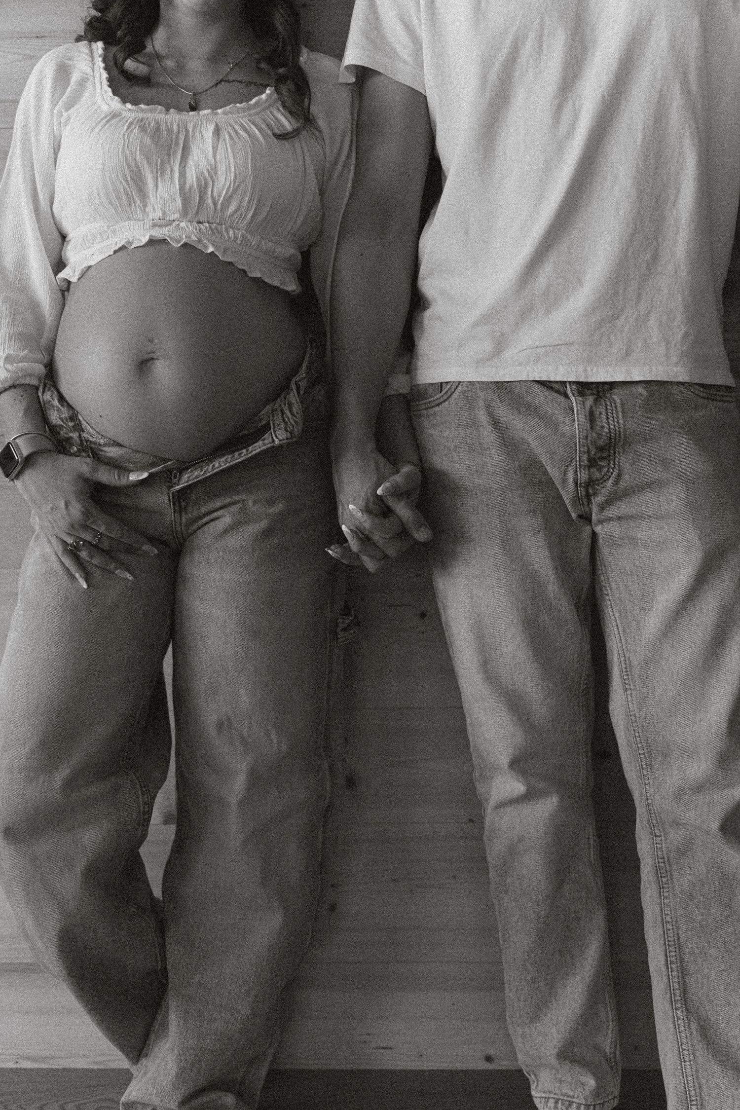 Black and white detail of a pregnant belly and the couple holding hands