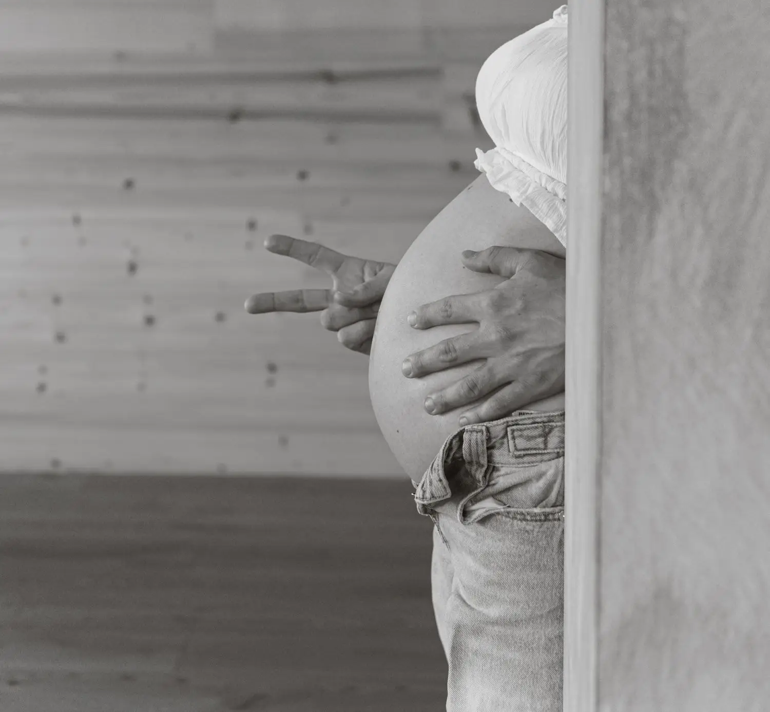 Black and white photo of a hand making a peace sign next to the baby bump
