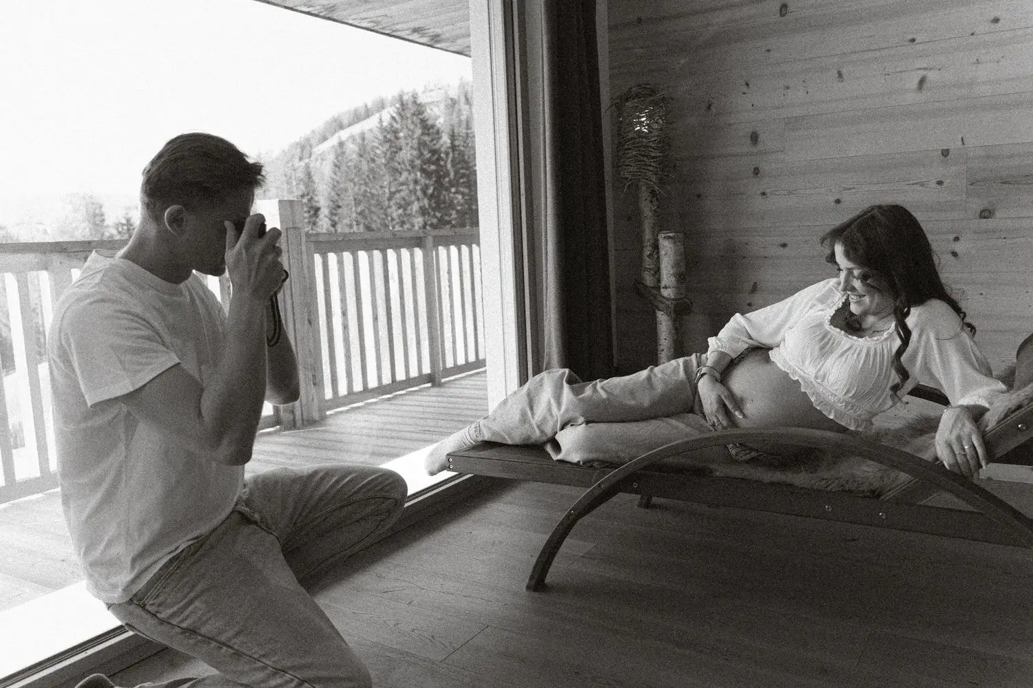 Black and white photo of a partner photographing the mother-to-be on a chalet terrace