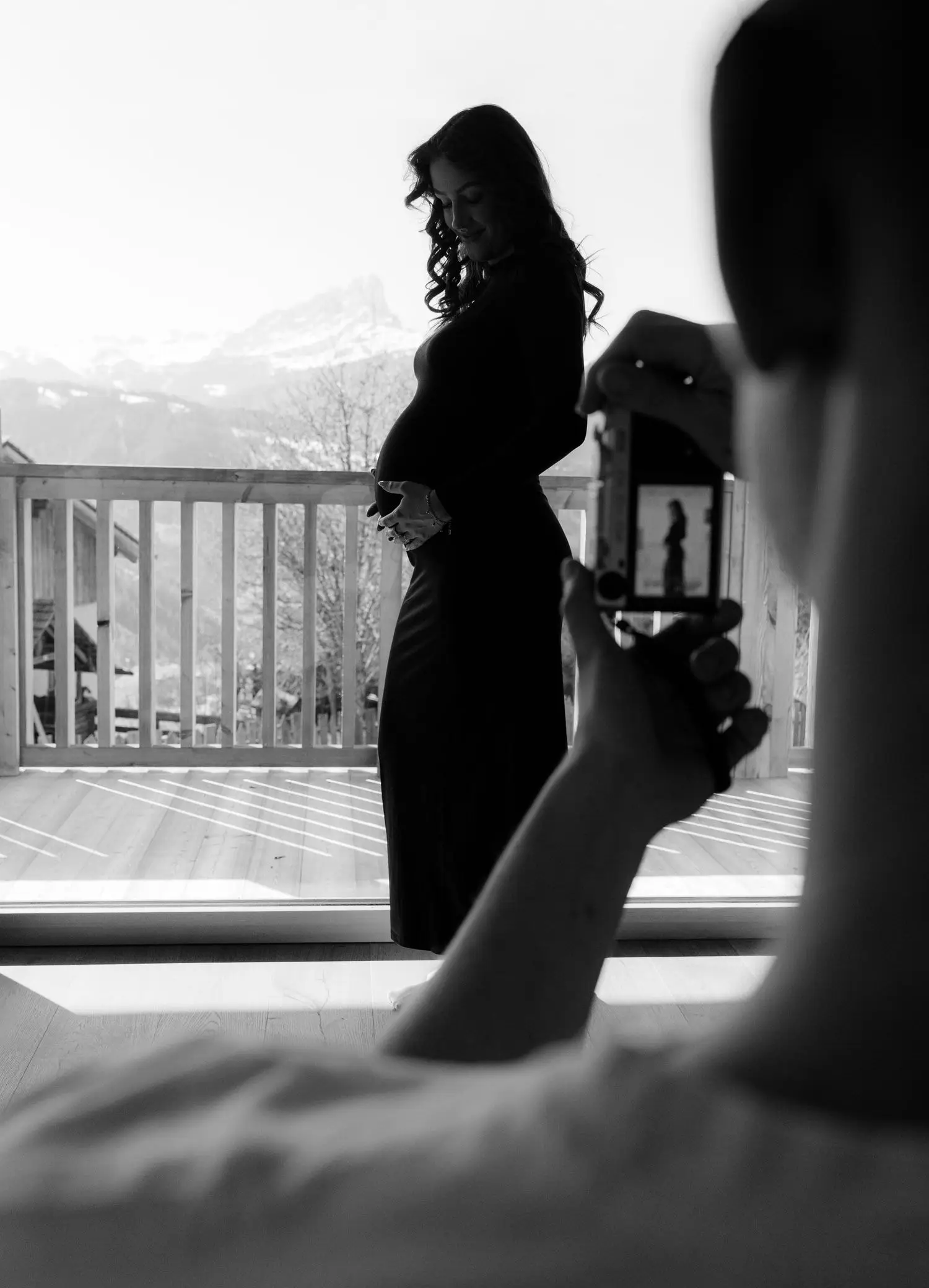 Black and white silhouette of a pregnant woman by a mountain window, photographed on a phone