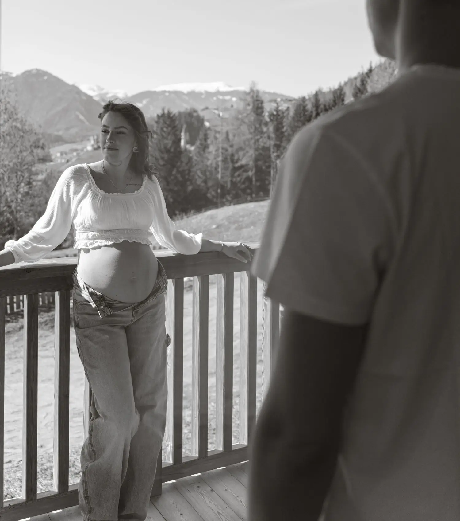 Black and white photo of the mother-to-be on a balcony with mountains behind