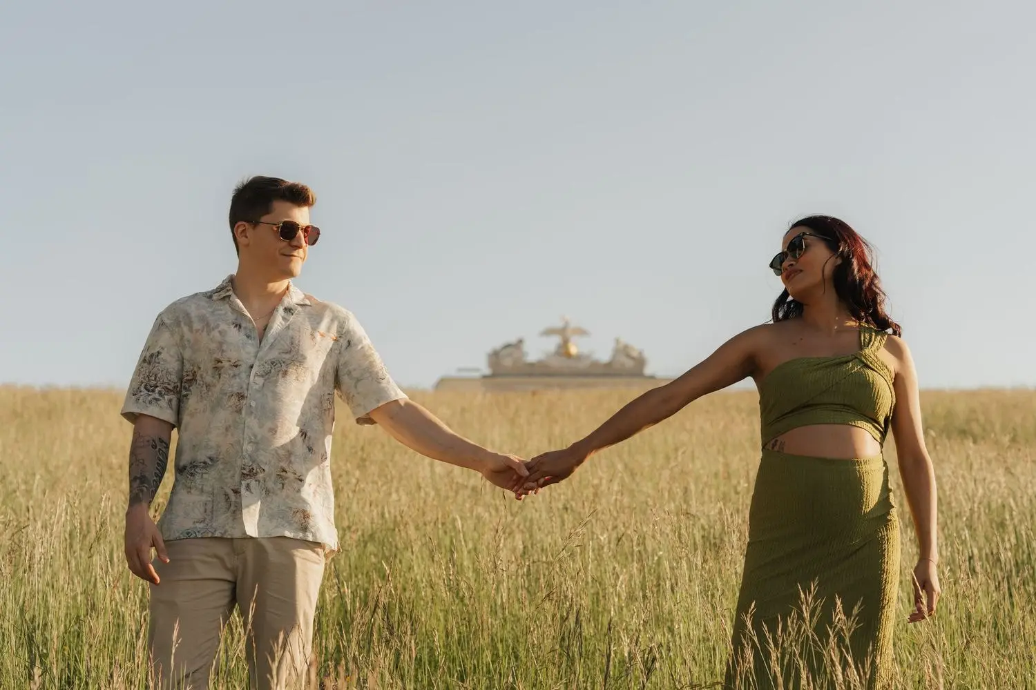 Couple holding hands in tall grass in front of the Gloriette in Vienna