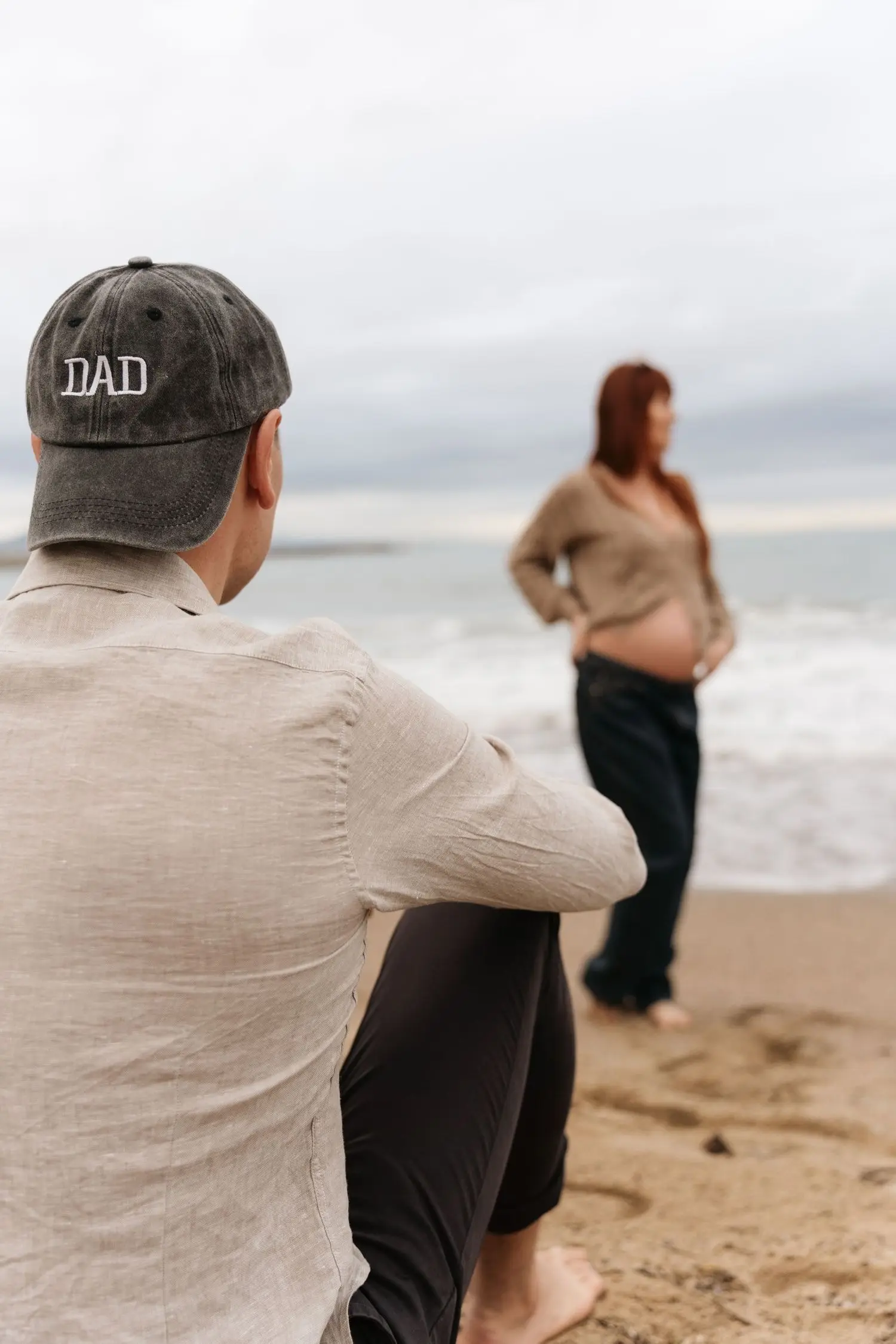 Expectant father in a DAD cap watching the mother-to-be by the sea
