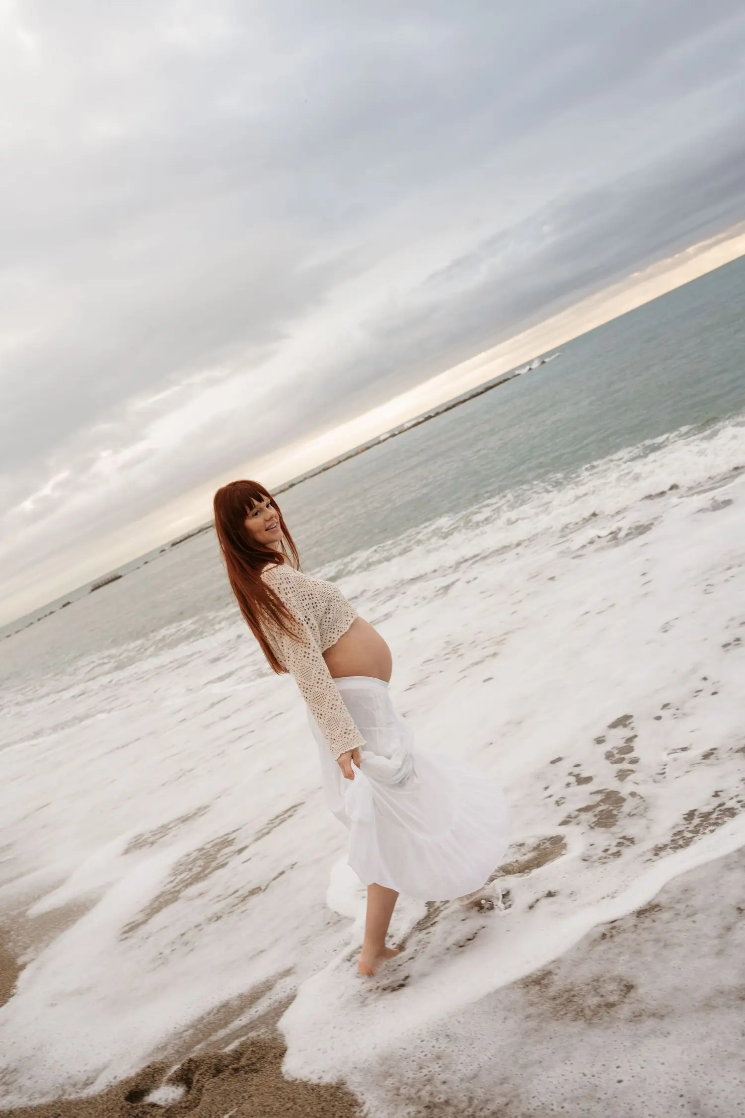 Mother-to-be in a white skirt standing in the surf