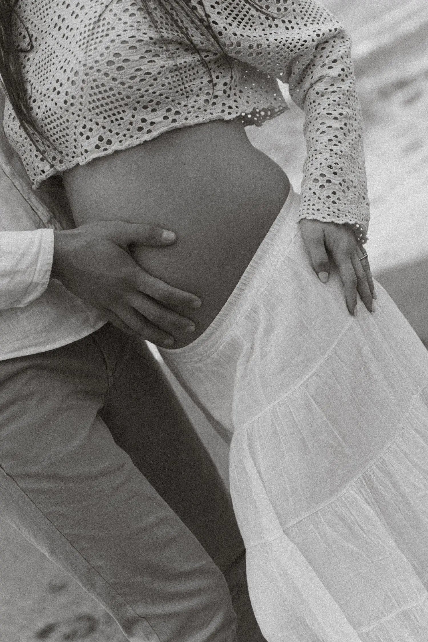 Black and white detail of hands on the baby bump and a flowing skirt