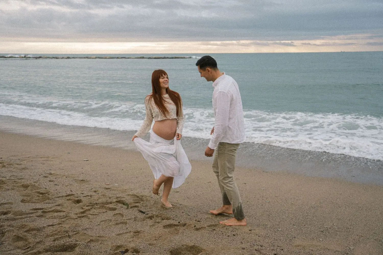 Mother-to-be twirling her skirt on the beach as he watches