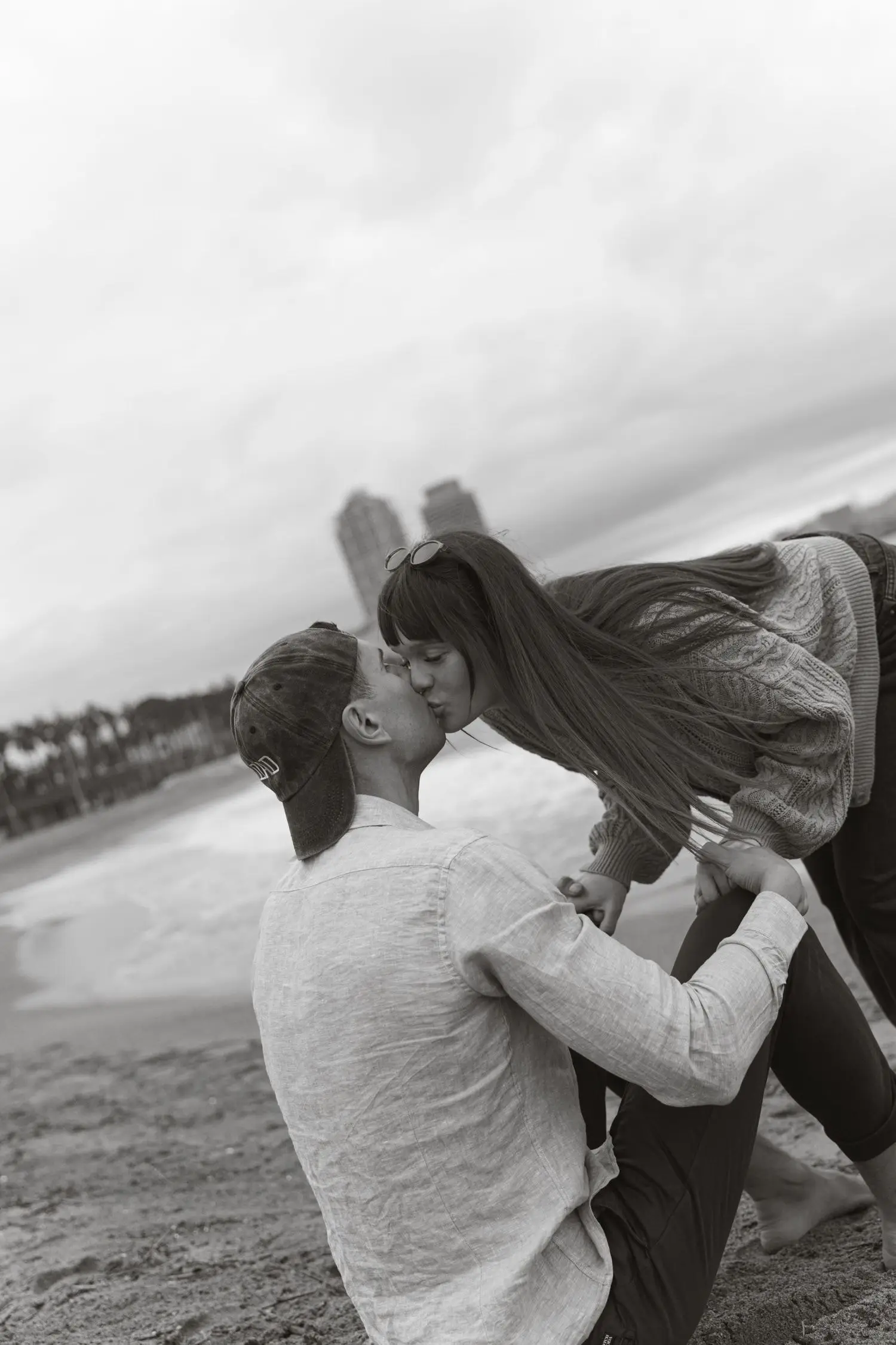 Black and white photo of the couple kissing on the beach in the wind