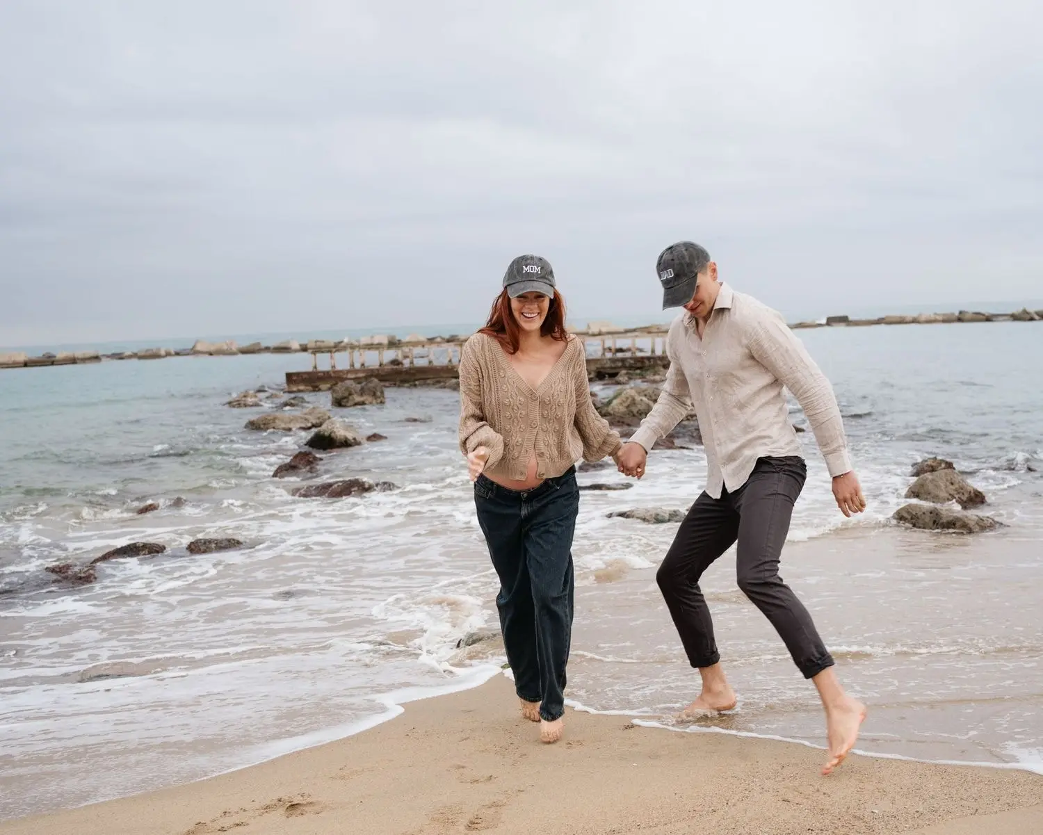 Couple in caps playing barefoot at the water's edge