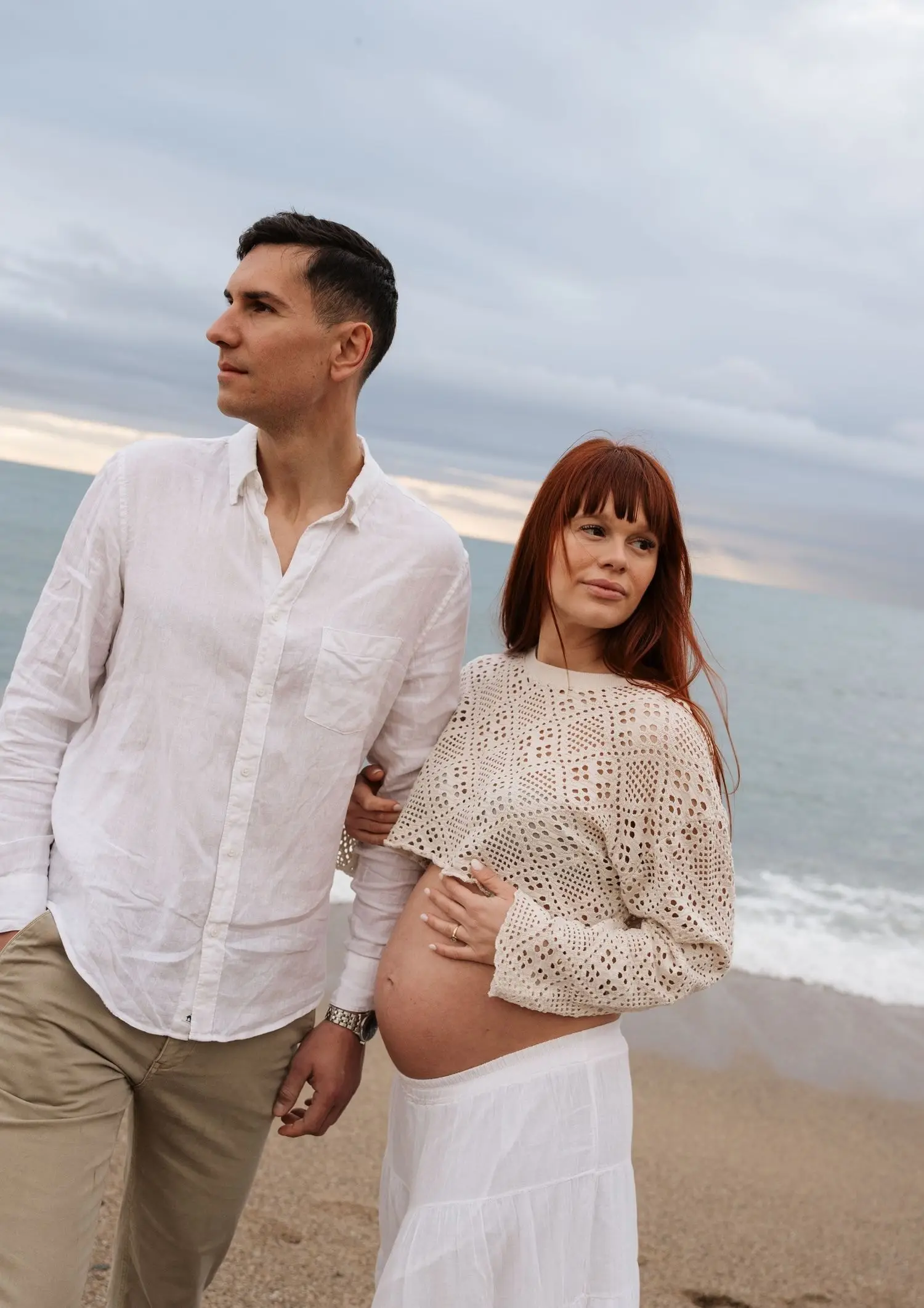 Couple walking arm in arm on the beach, she in a crochet top