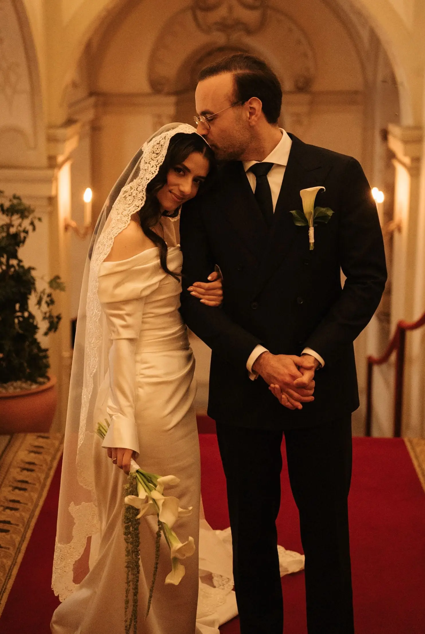 Groom kisses the bride's forehead on the red carpet in the palace