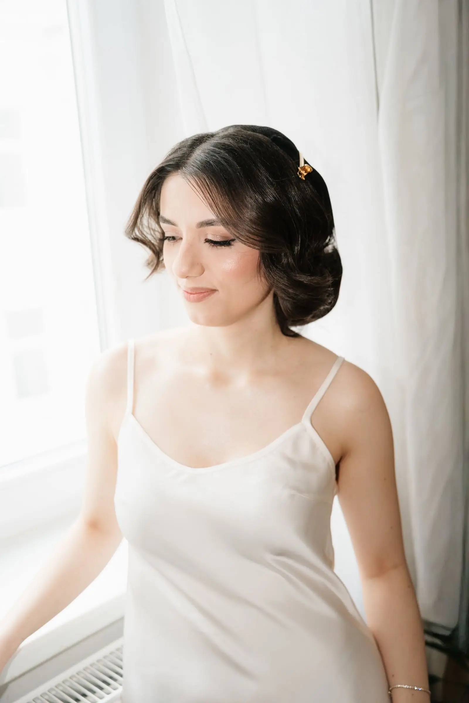 Bride in a silk slip dress getting ready by the window