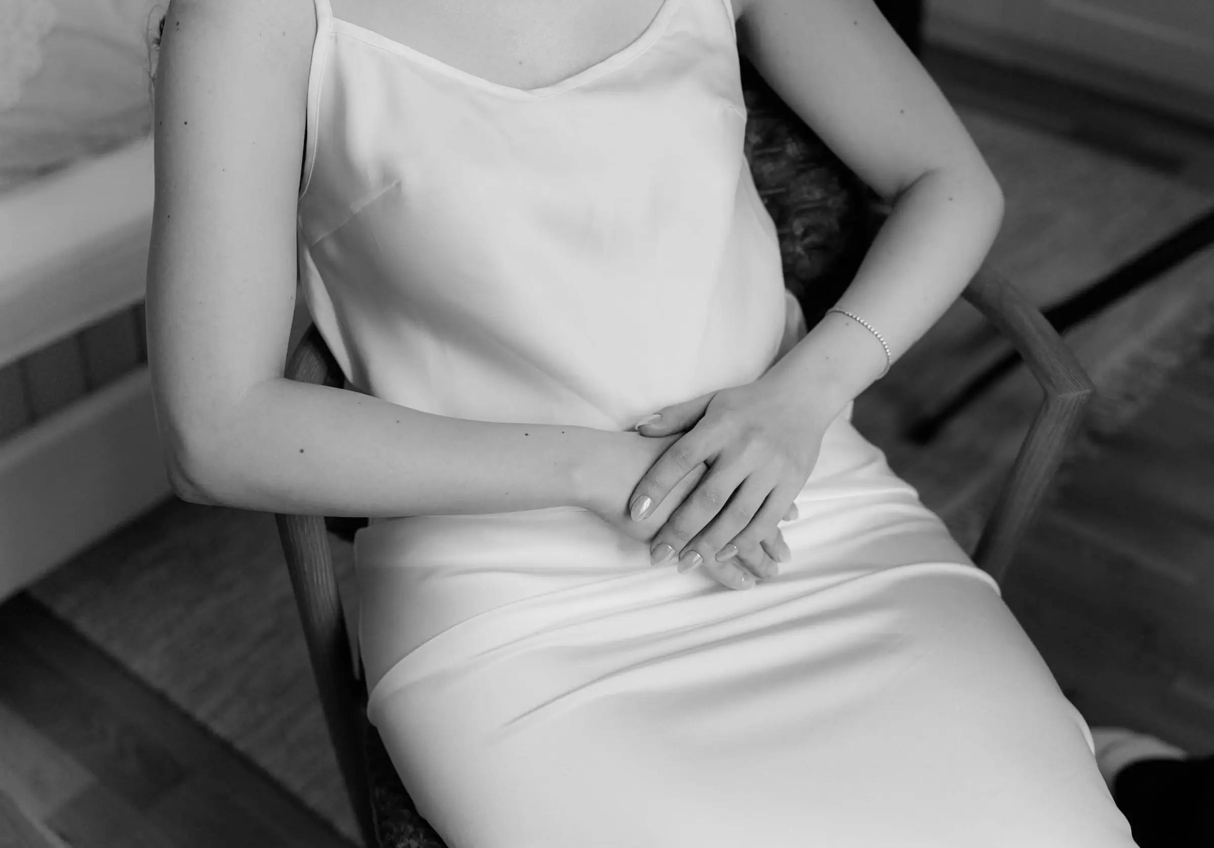 Black and white detail of the bride's hands on her silk dress