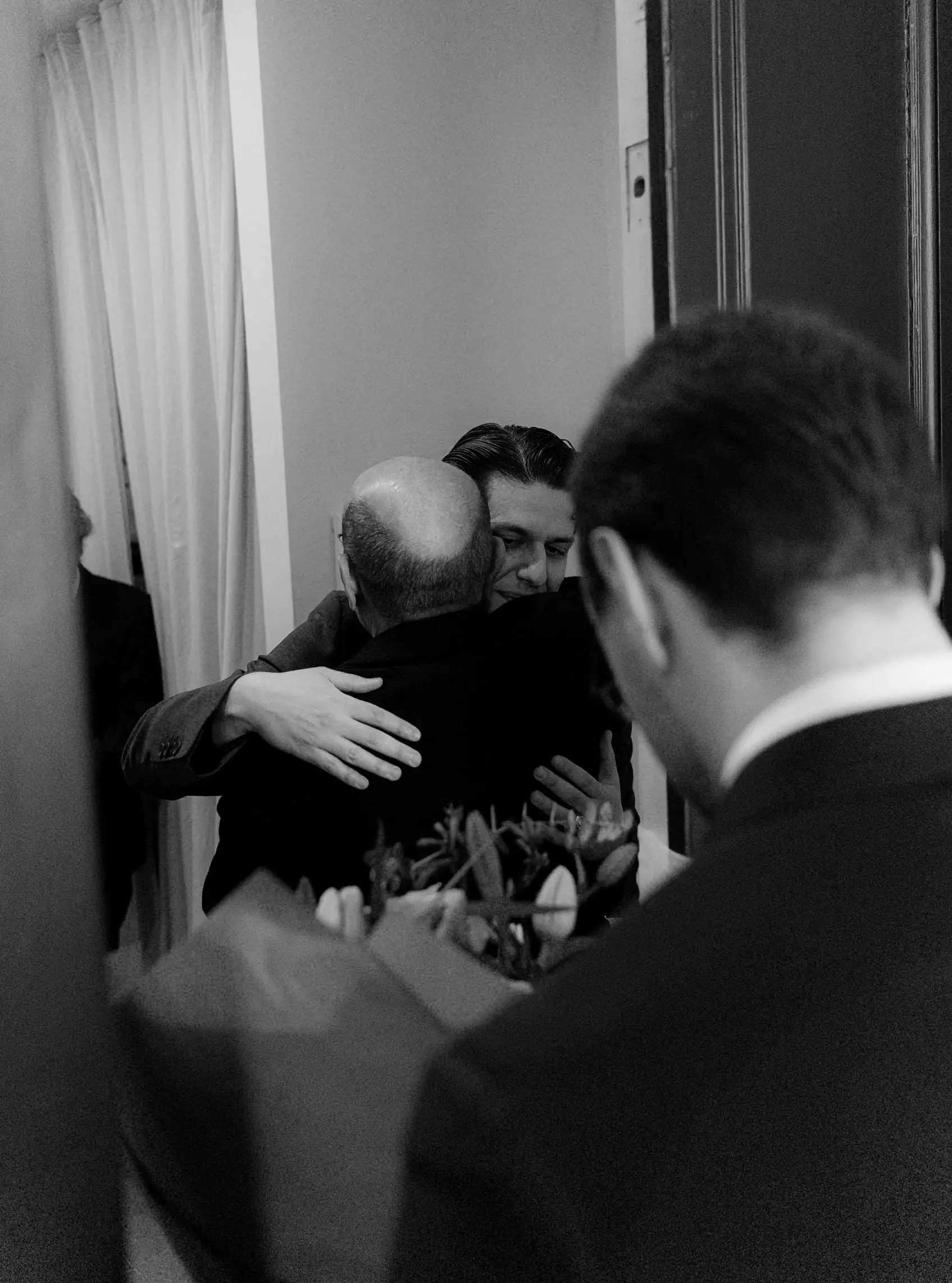 Black and white photo of the groom being hugged at the door