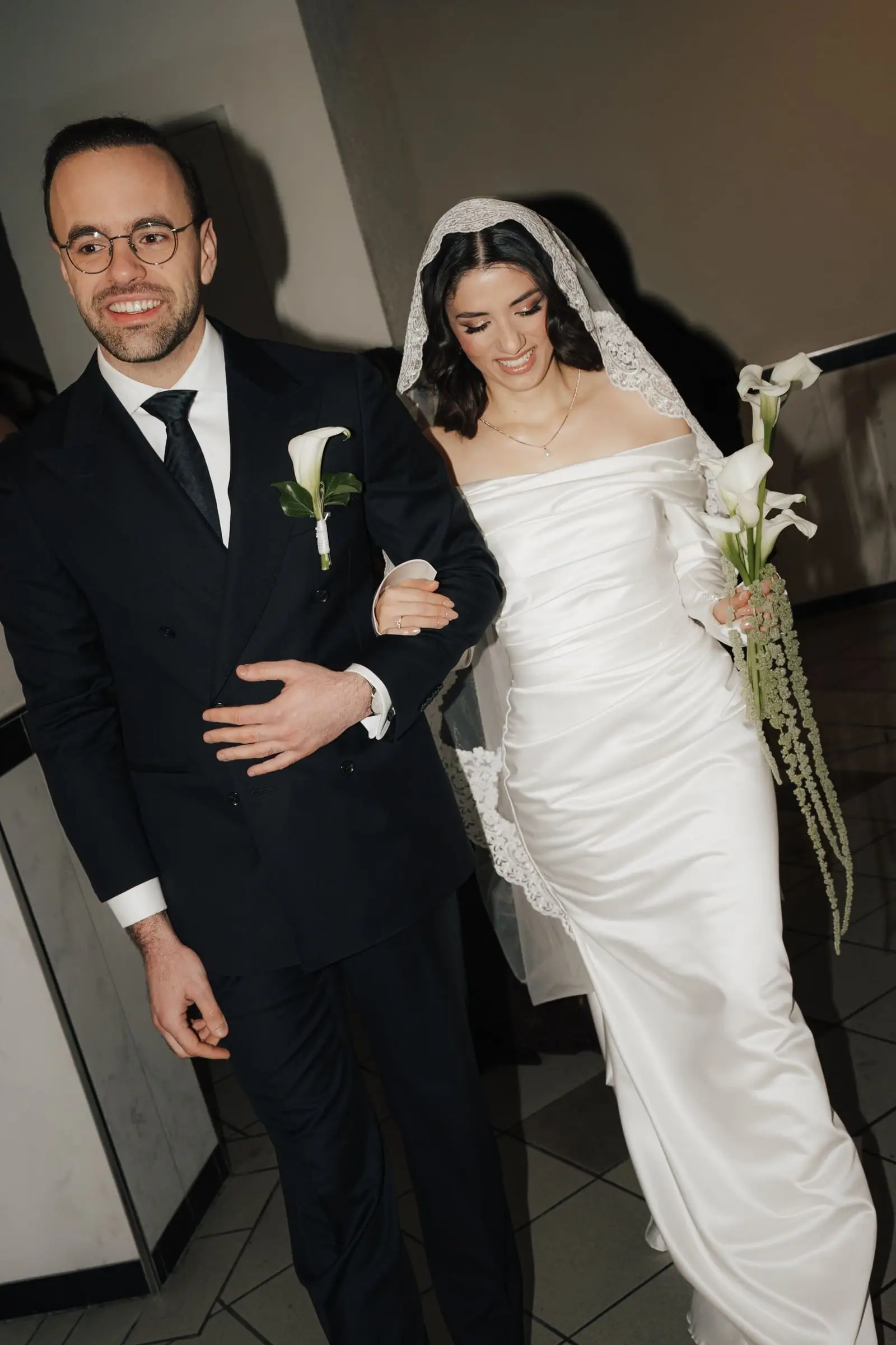 Groom and bride walking arm in arm, calla lilies in her hand