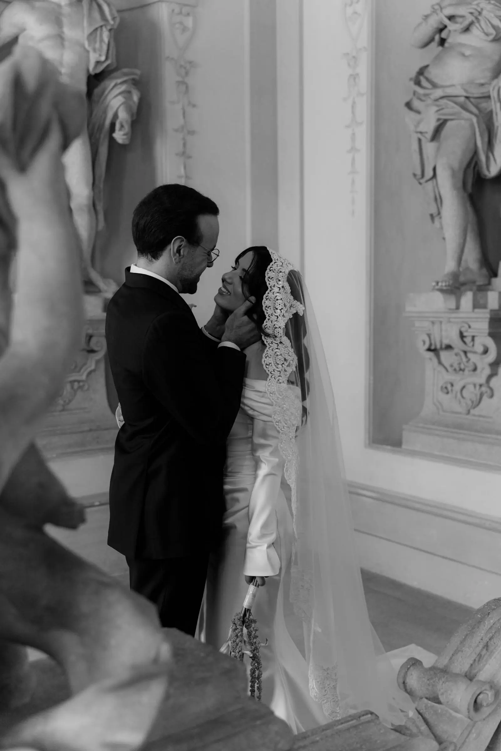 Black and white photo of the couple kissing between stucco sculptures