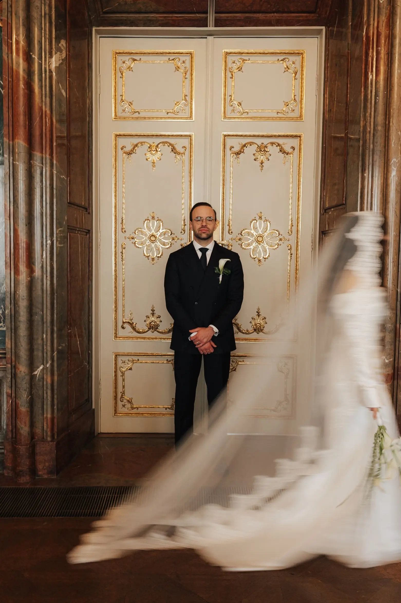 Bride hurries towards the groom at a gilded door, her veil in motion