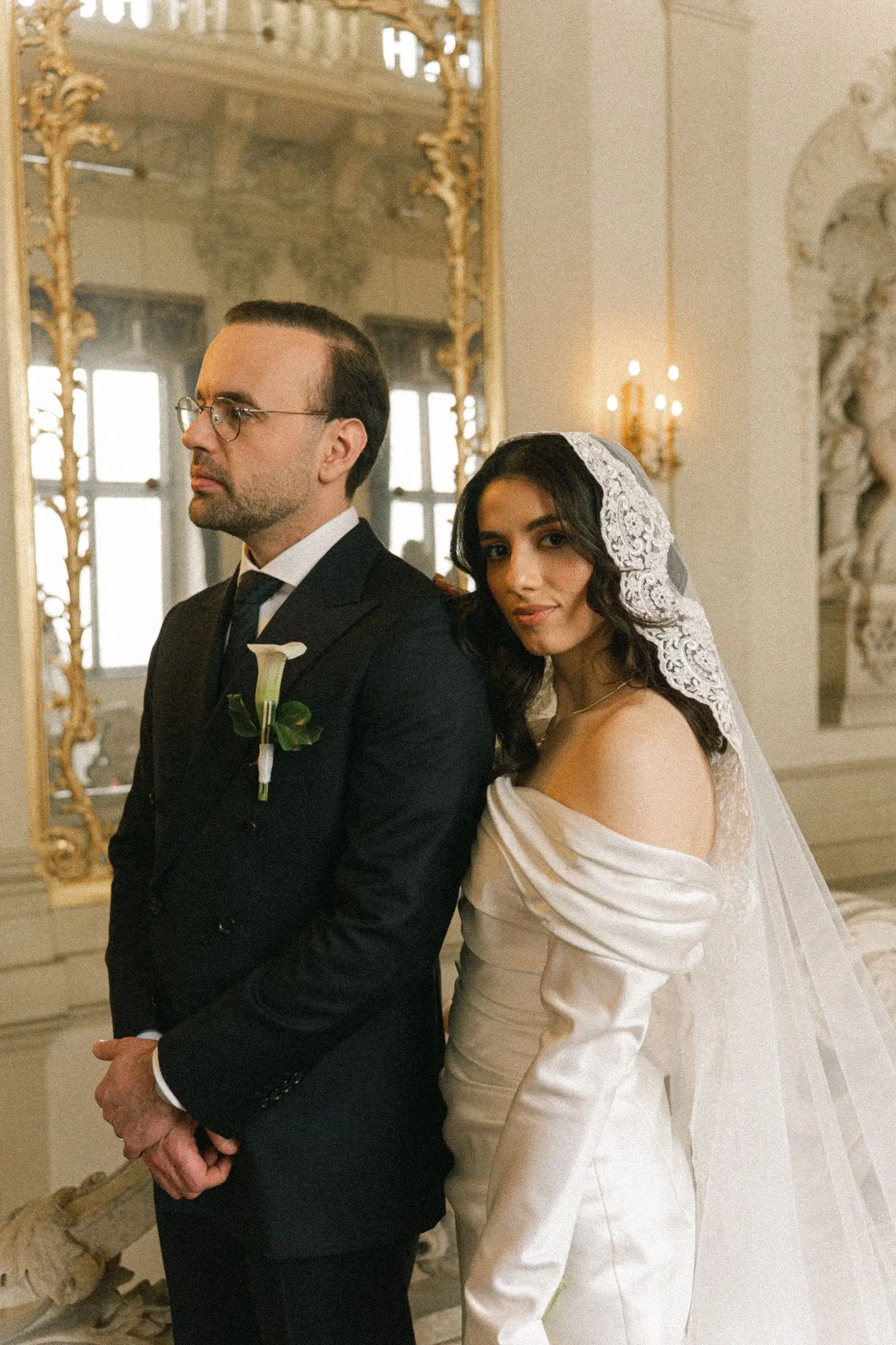 Portrait of the couple by a gilded mirror and wall sconces