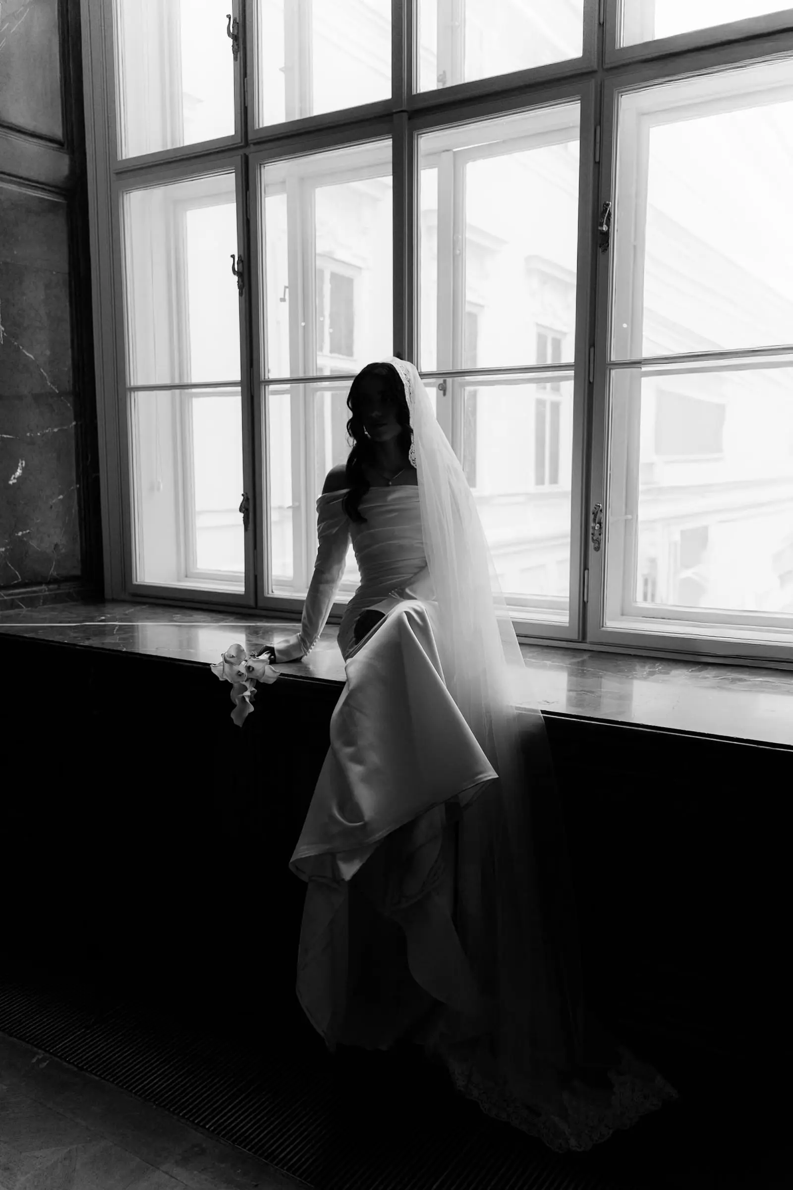 Black and white photo of the bride sitting on a tall window sill