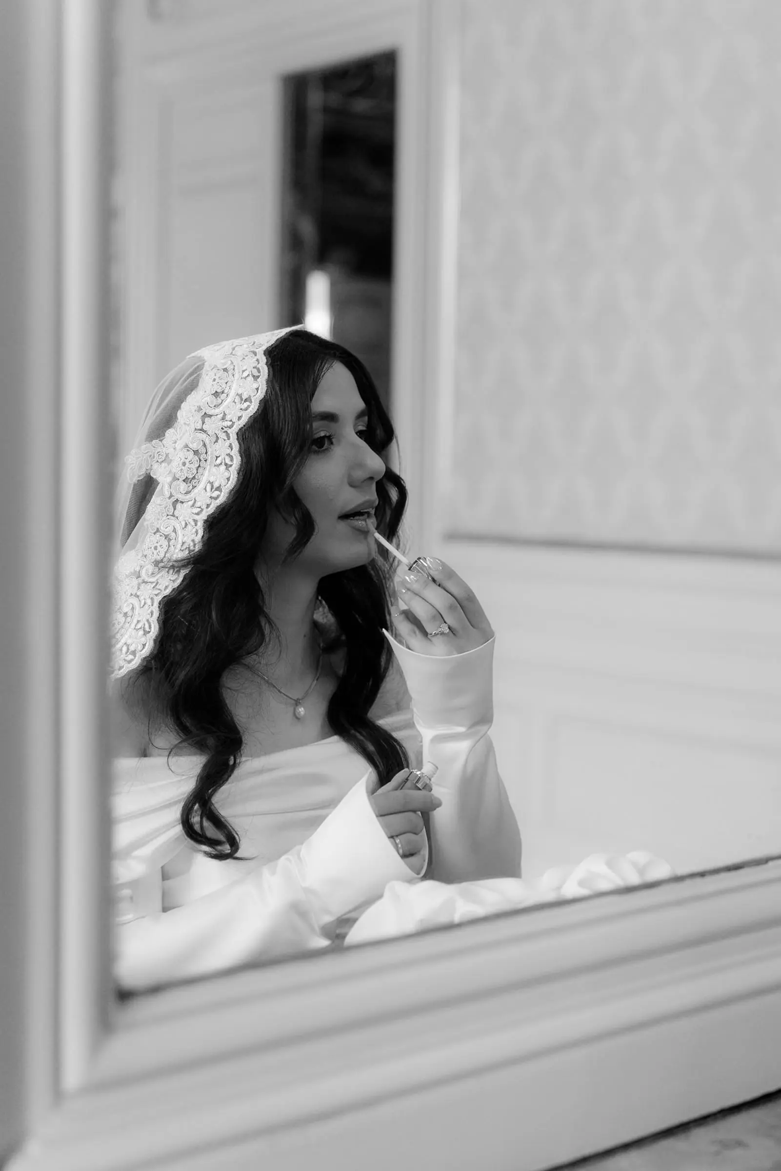 Black and white photo of the bride putting on lipstick in the mirror