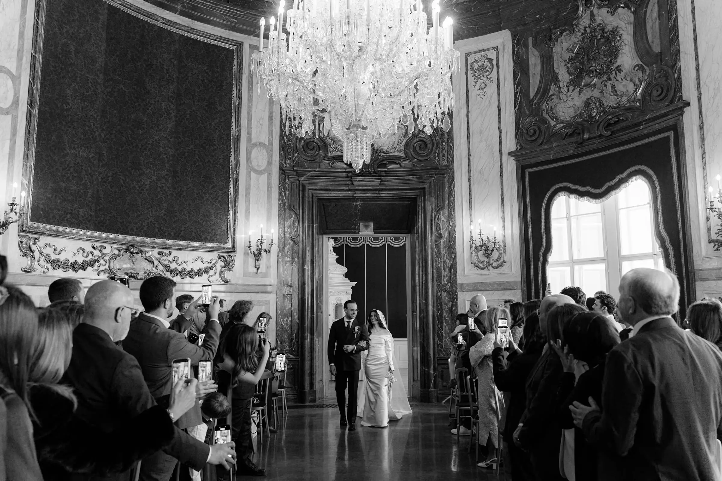 Black and white photo of the couple walking down the aisle in the palace hall
