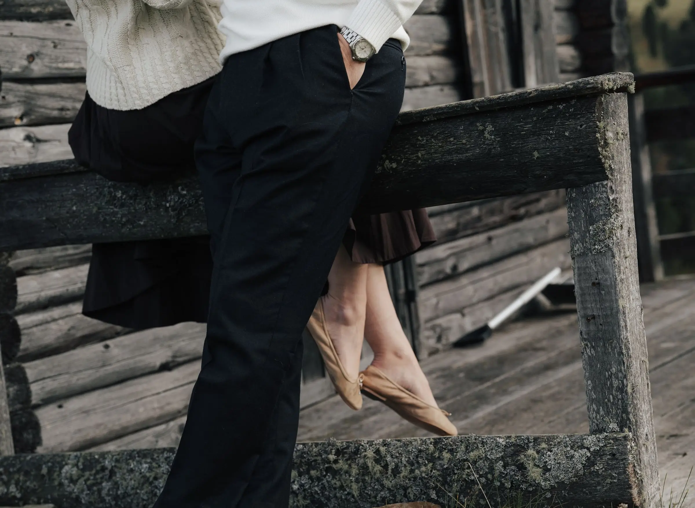 Detail of the couple sitting on the wooden railing of an old mountain hut