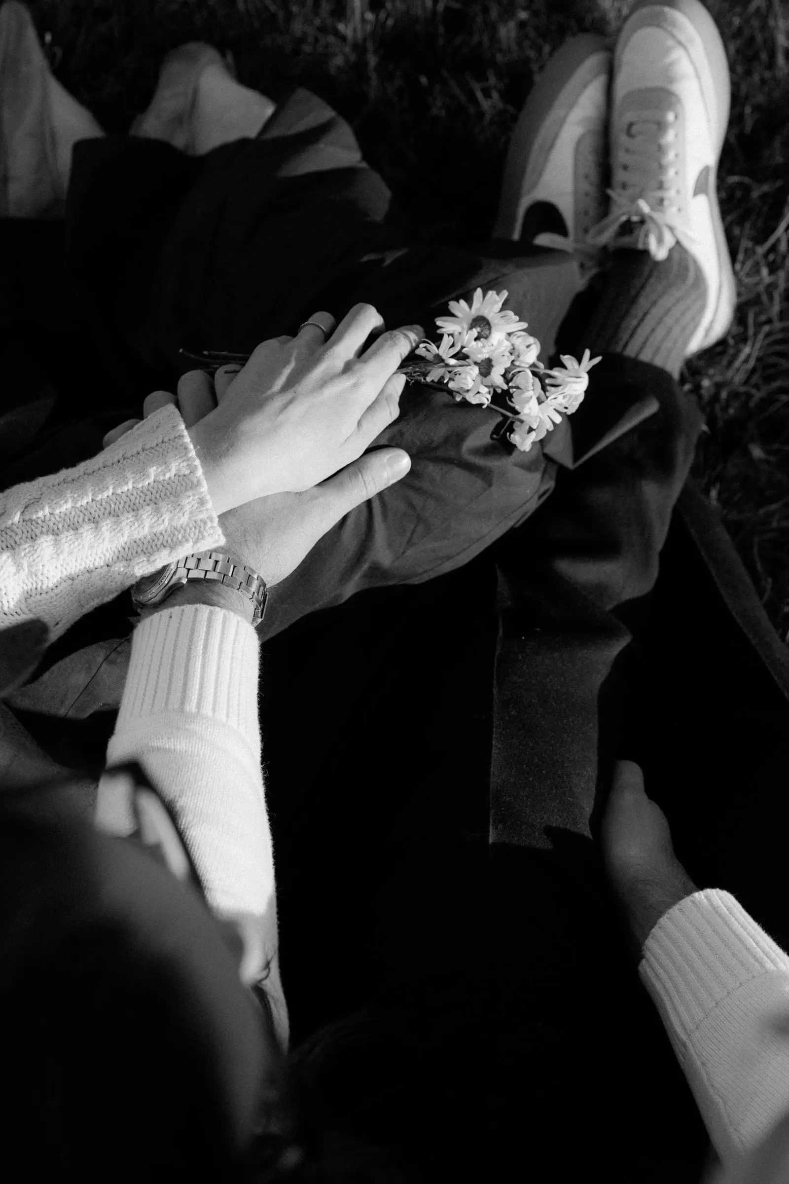 Black and white detail of hands, knit sweaters and a small bunch of daisies