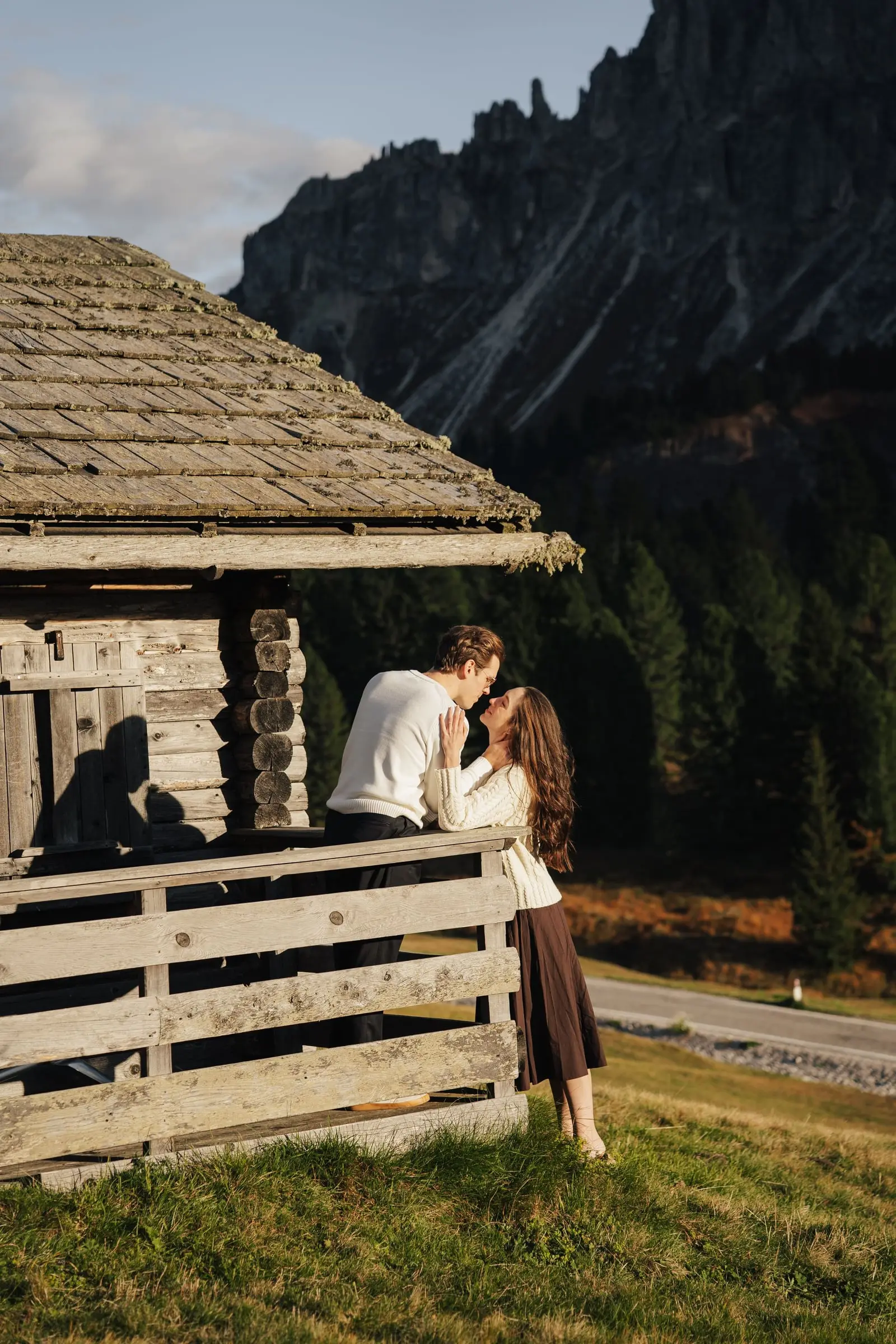 Couple kissing on the porch of a wooden hut at Passo delle Erbe, Sass de Putia behind