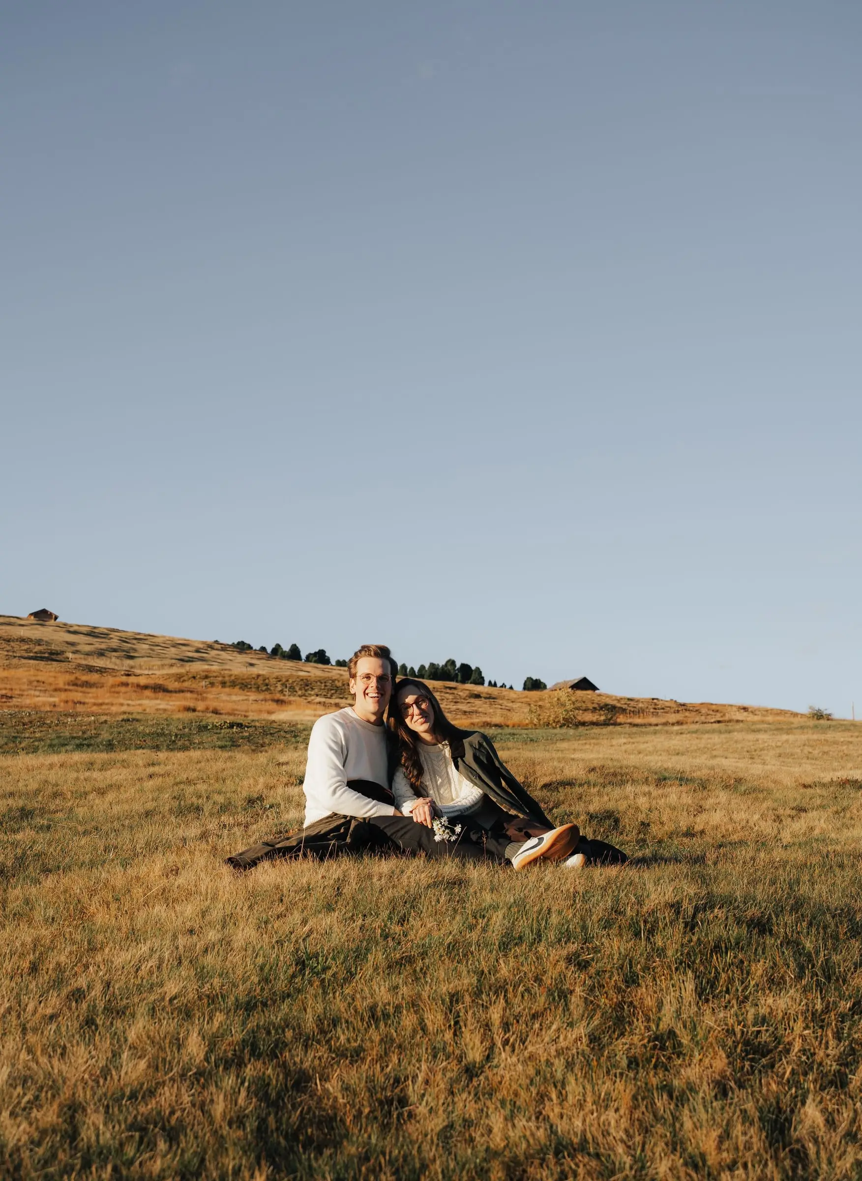 Couple sitting together in the golden grass of an alpine meadow