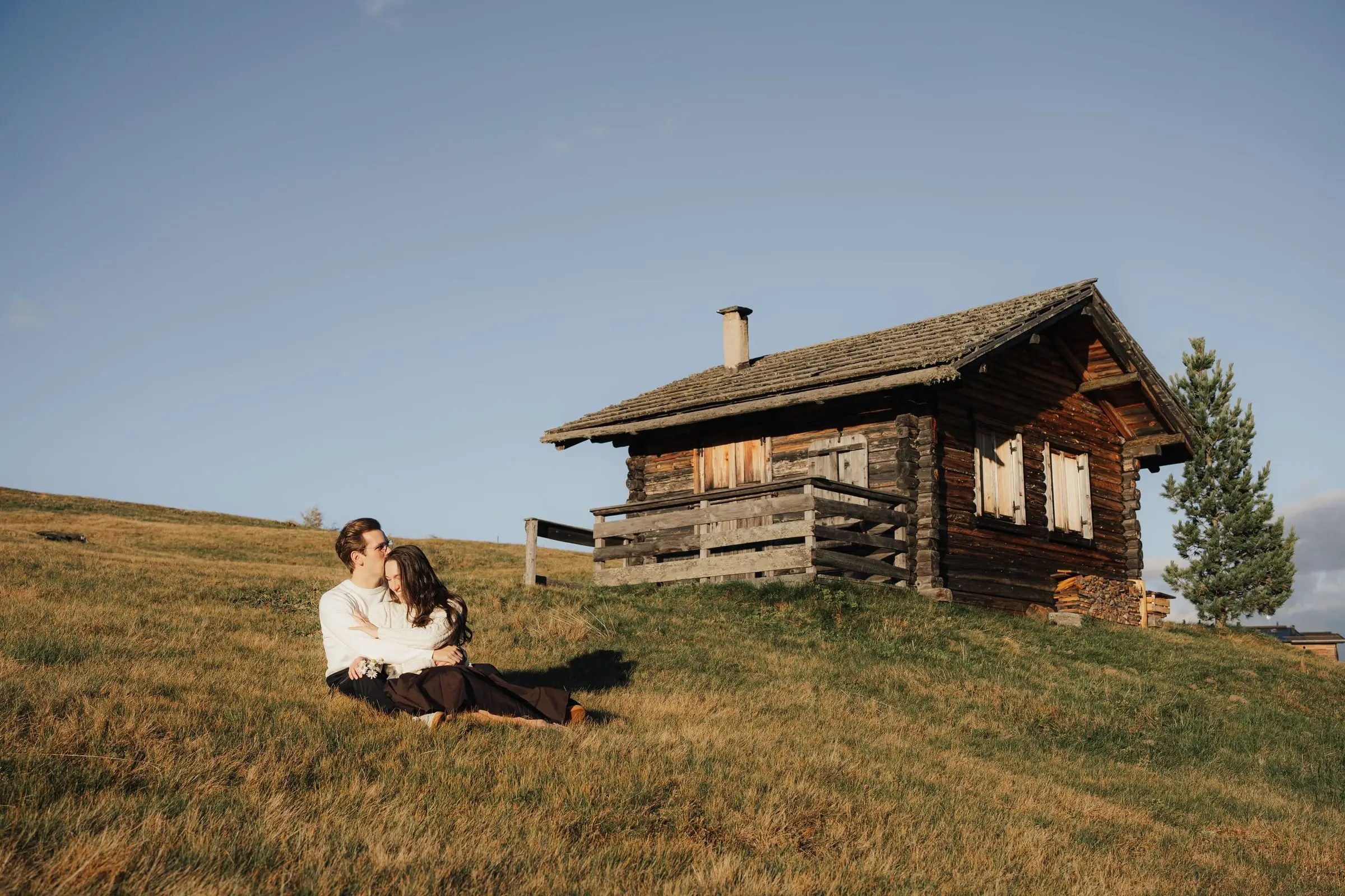 Couple sitting in the grass next to a wooden mountain hut