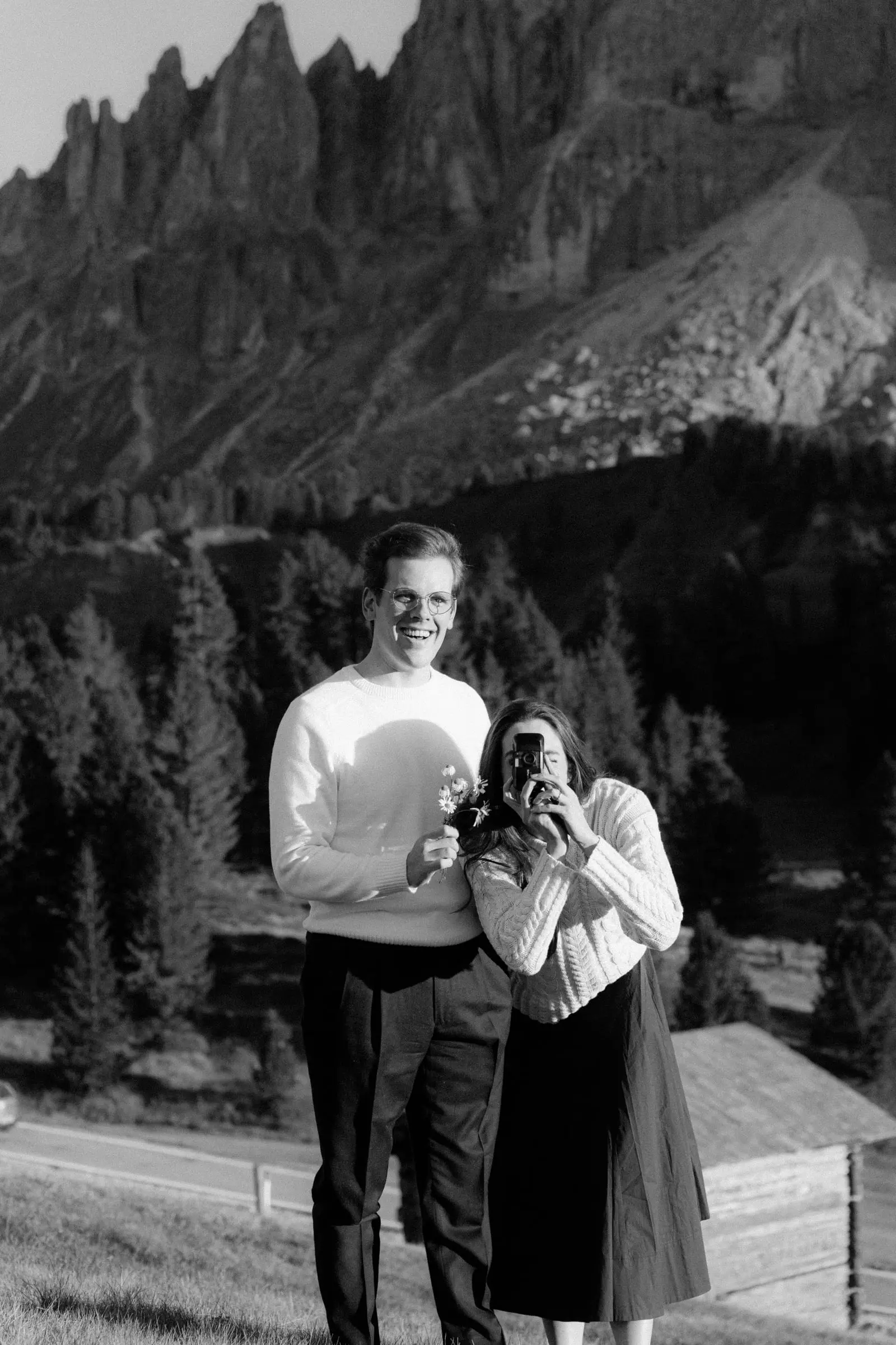 Black and white photo of the couple laughing as she takes a photo with a film camera