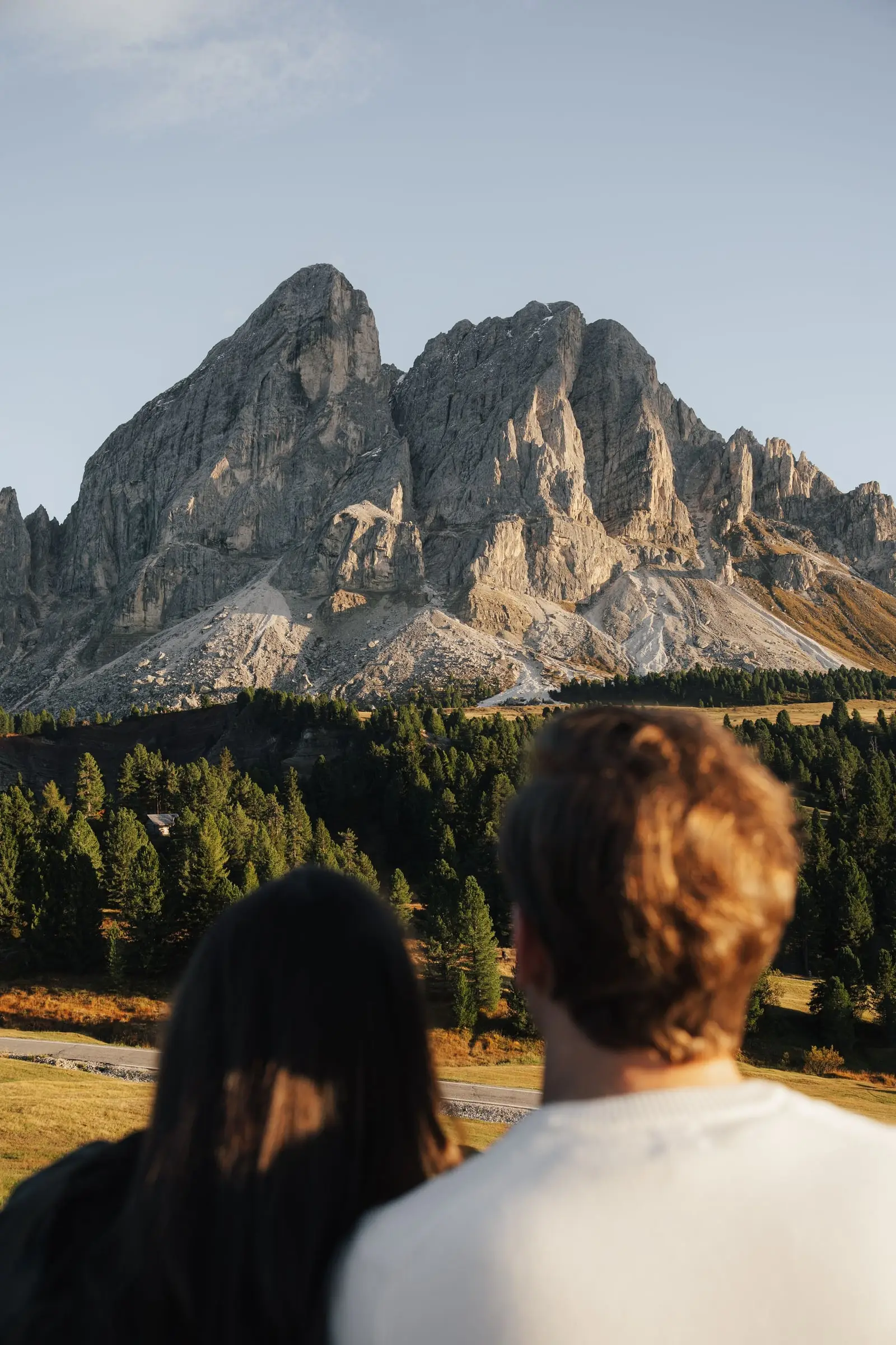 Couple seen from behind looking up at the Sass de Putia in golden light